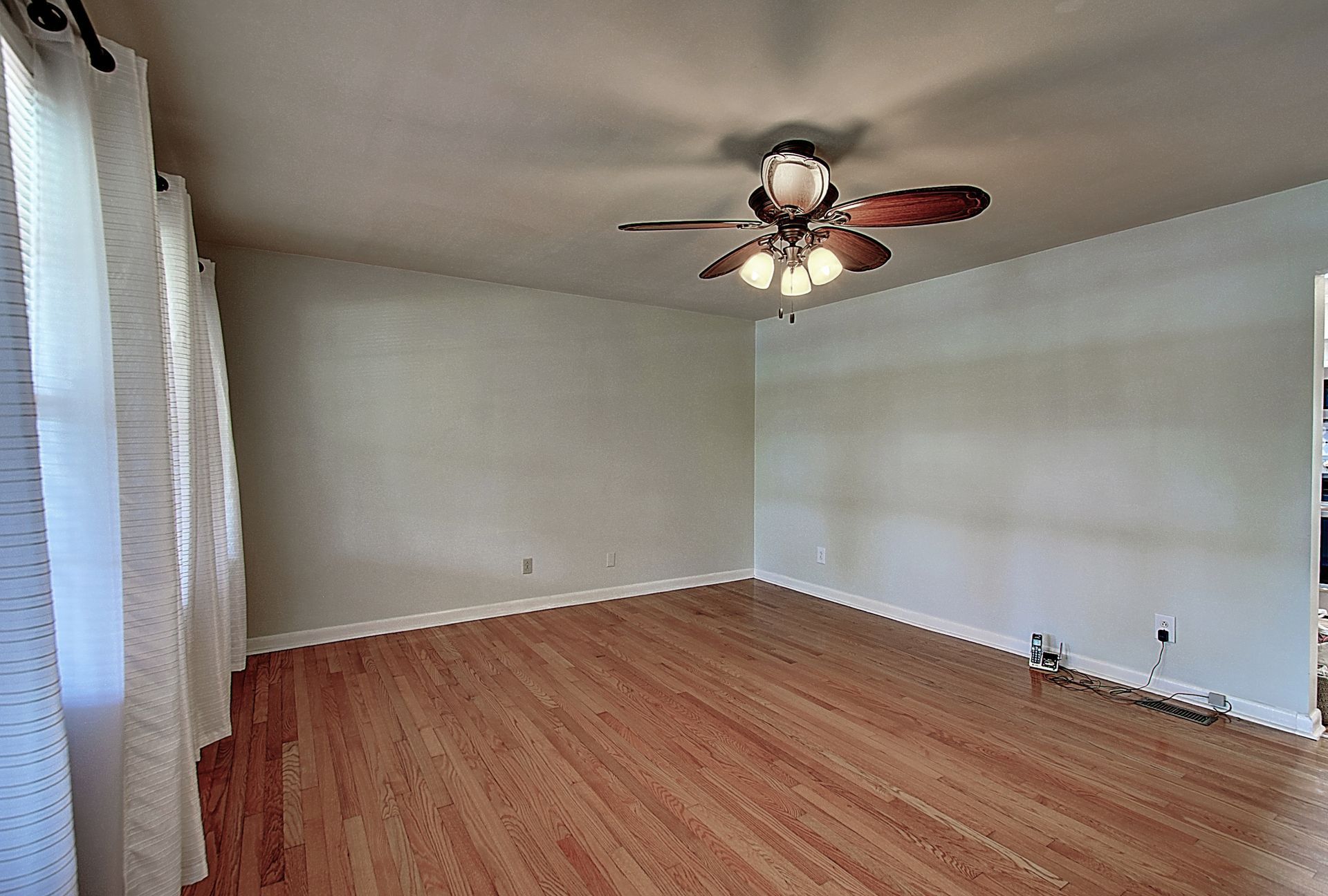An empty living room with hardwood floors and a ceiling fan.