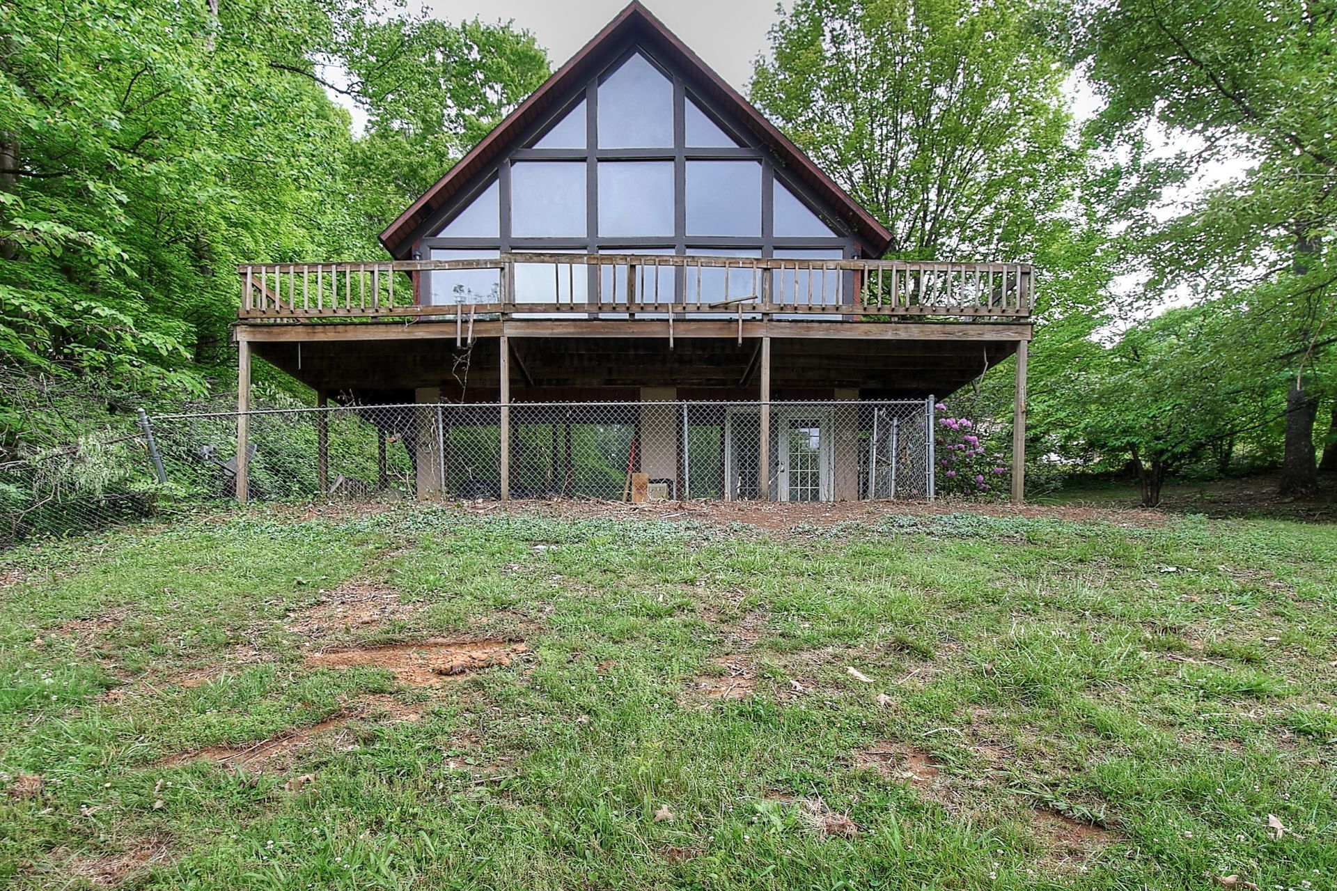 A large house with a large deck is surrounded by trees and grass.