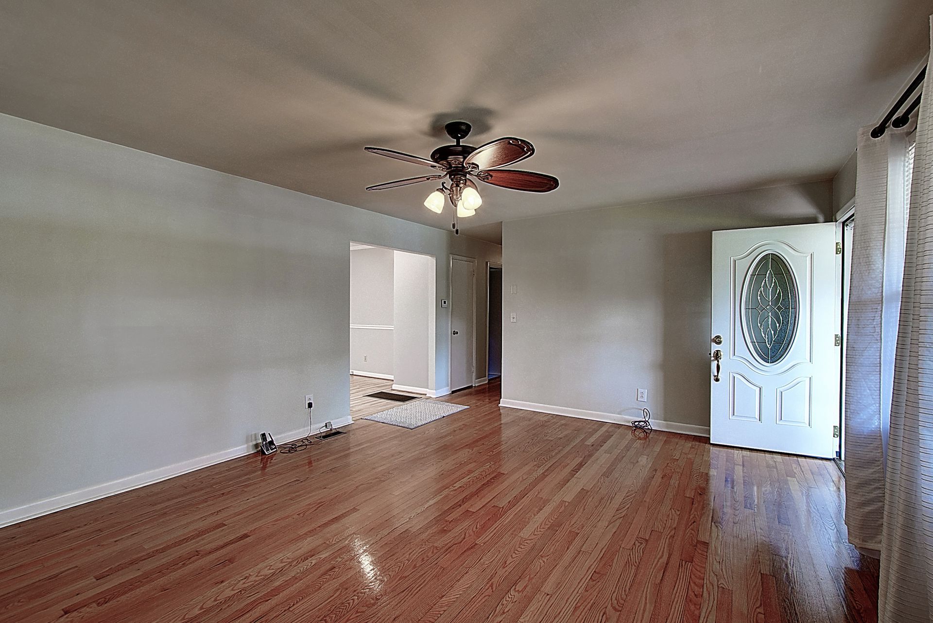 An empty living room with hardwood floors and a ceiling fan.