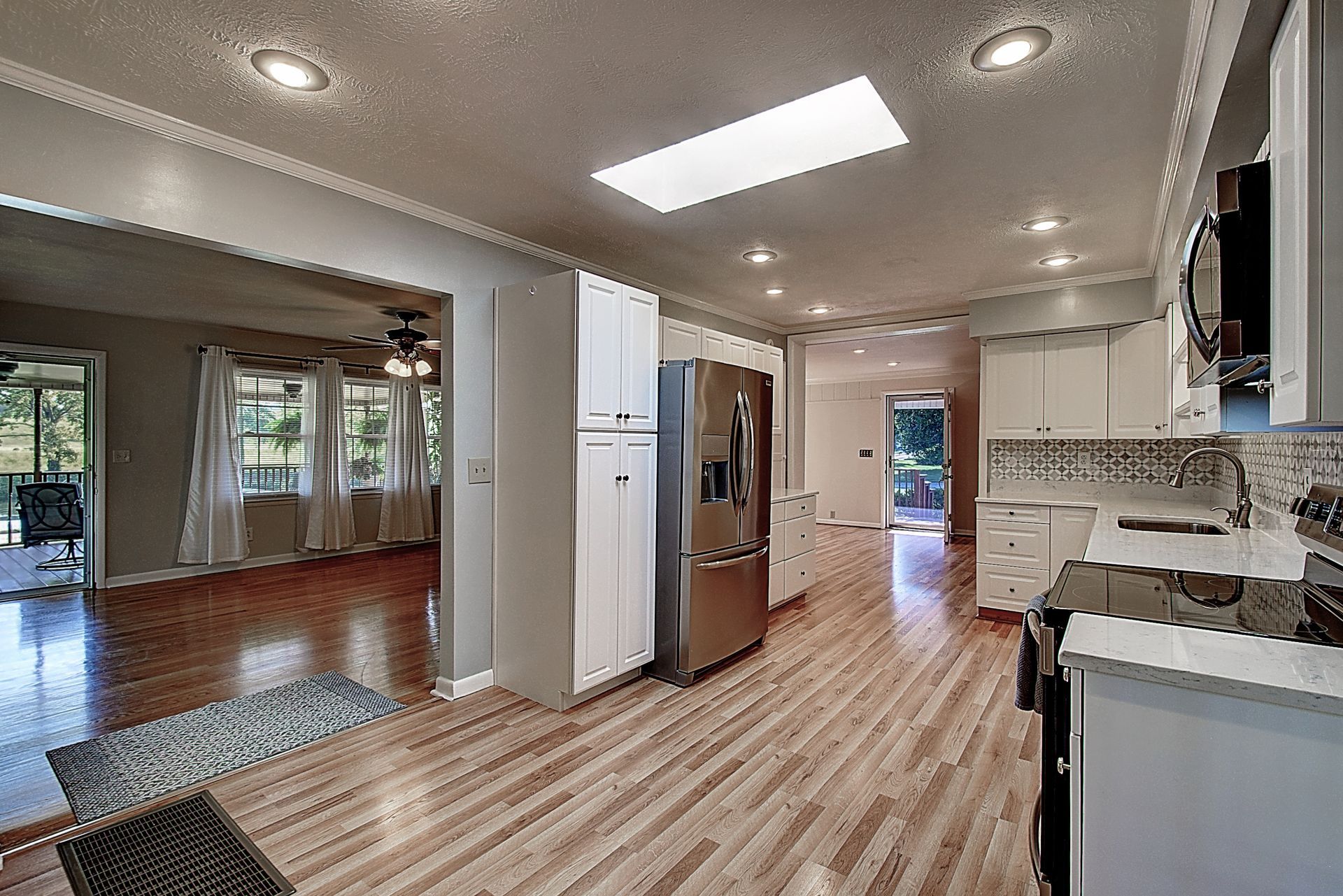A kitchen with hardwood floors , white cabinets , stainless steel appliances and a refrigerator.