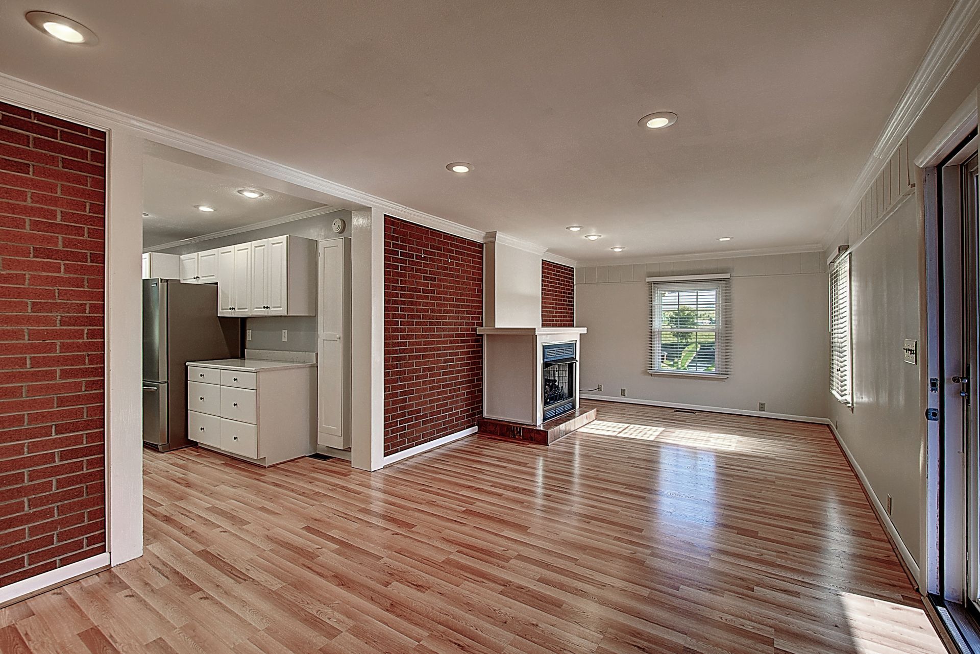 An empty living room with hardwood floors and a brick wall