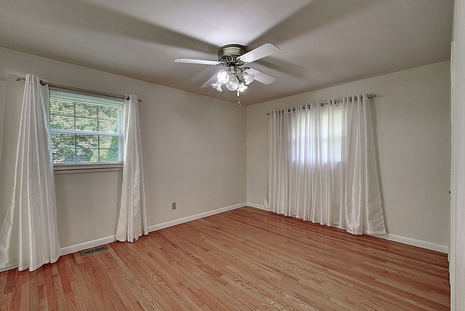An empty living room with hardwood floors and a ceiling fan.