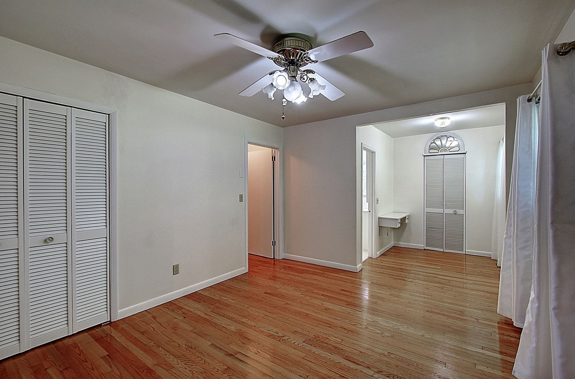 An empty room with hardwood floors and a ceiling fan