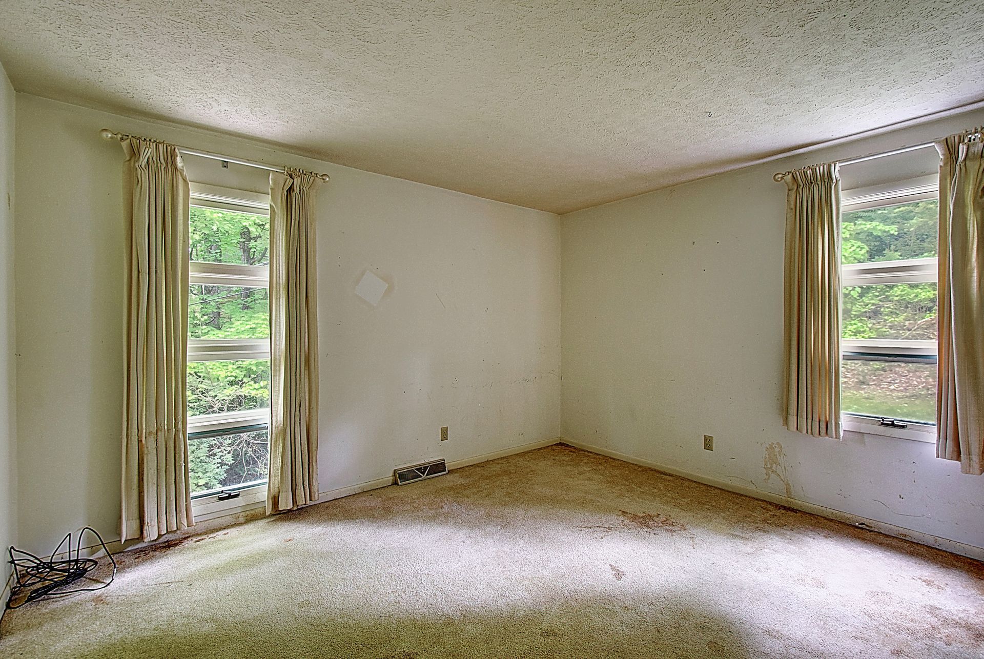 An empty room with a carpeted floor and two windows.
