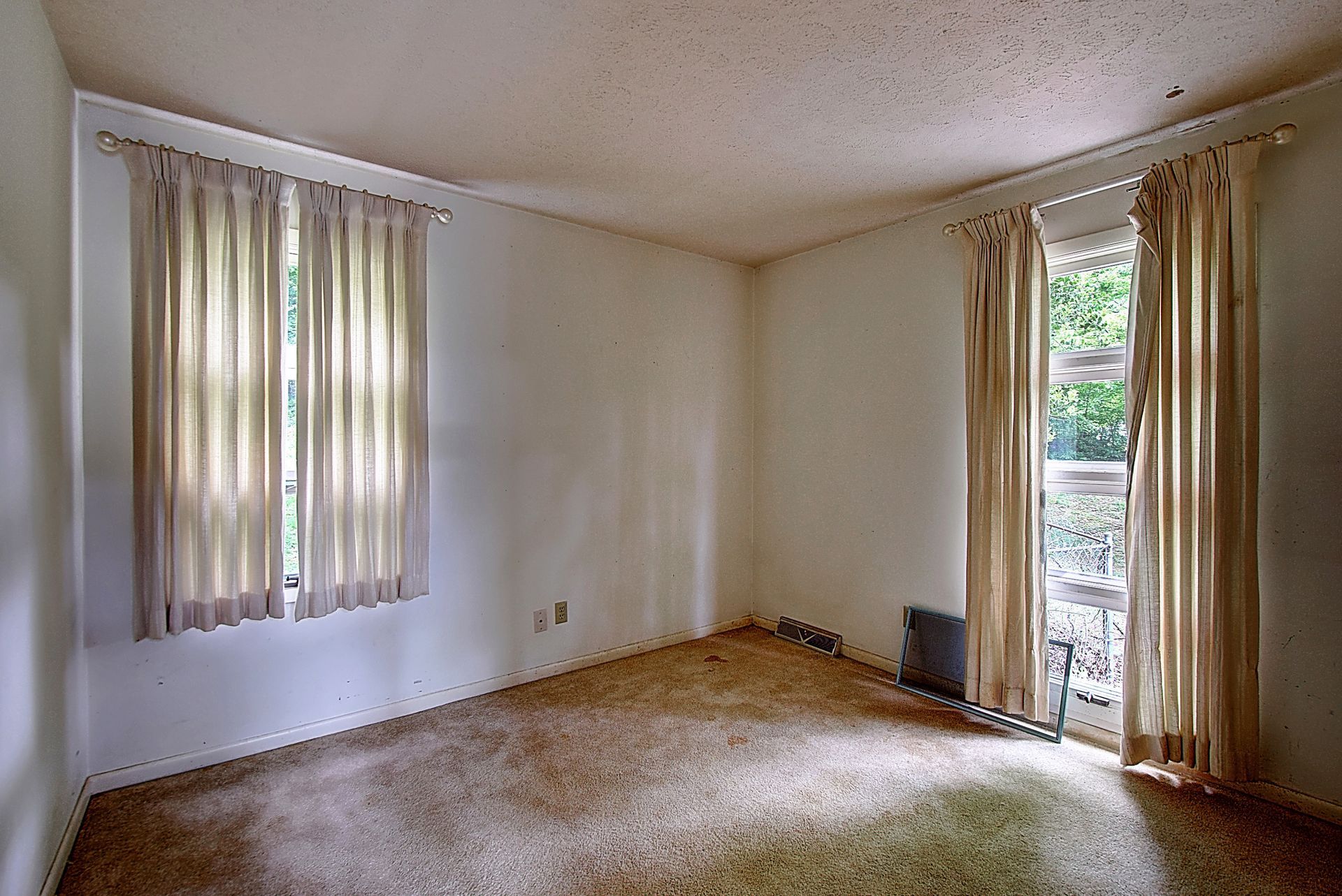 An empty living room with a carpeted floor and two windows.