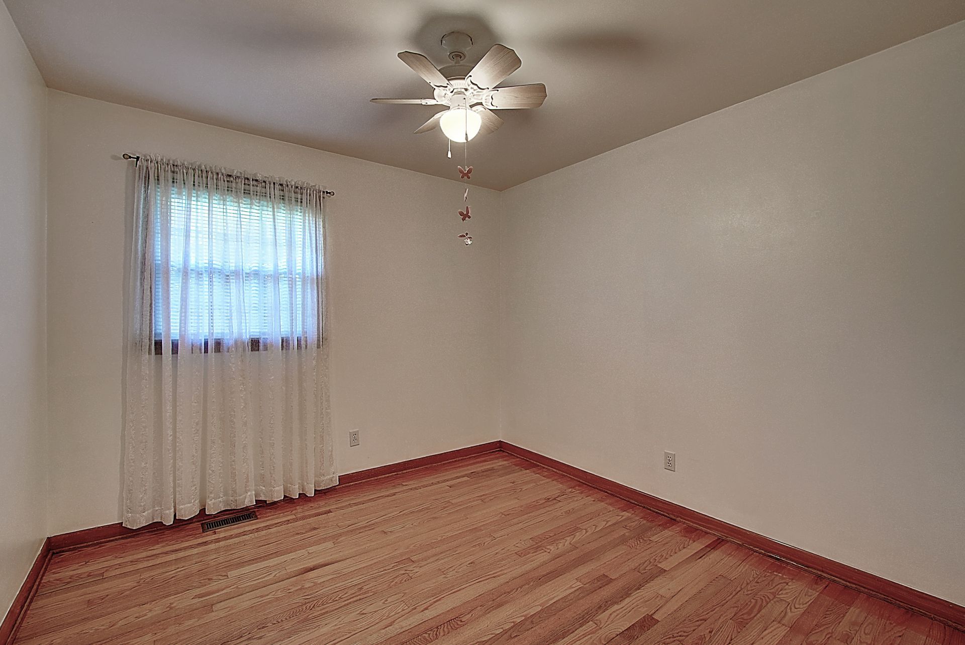 An empty bedroom with hardwood floors and a ceiling fan