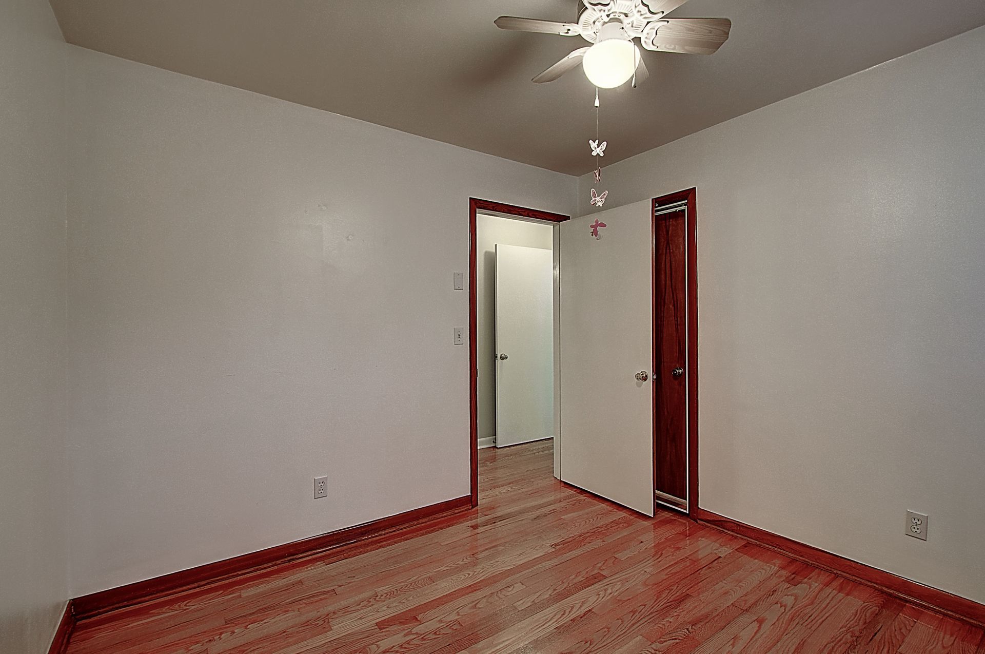 An empty bedroom with hardwood floors and a ceiling fan