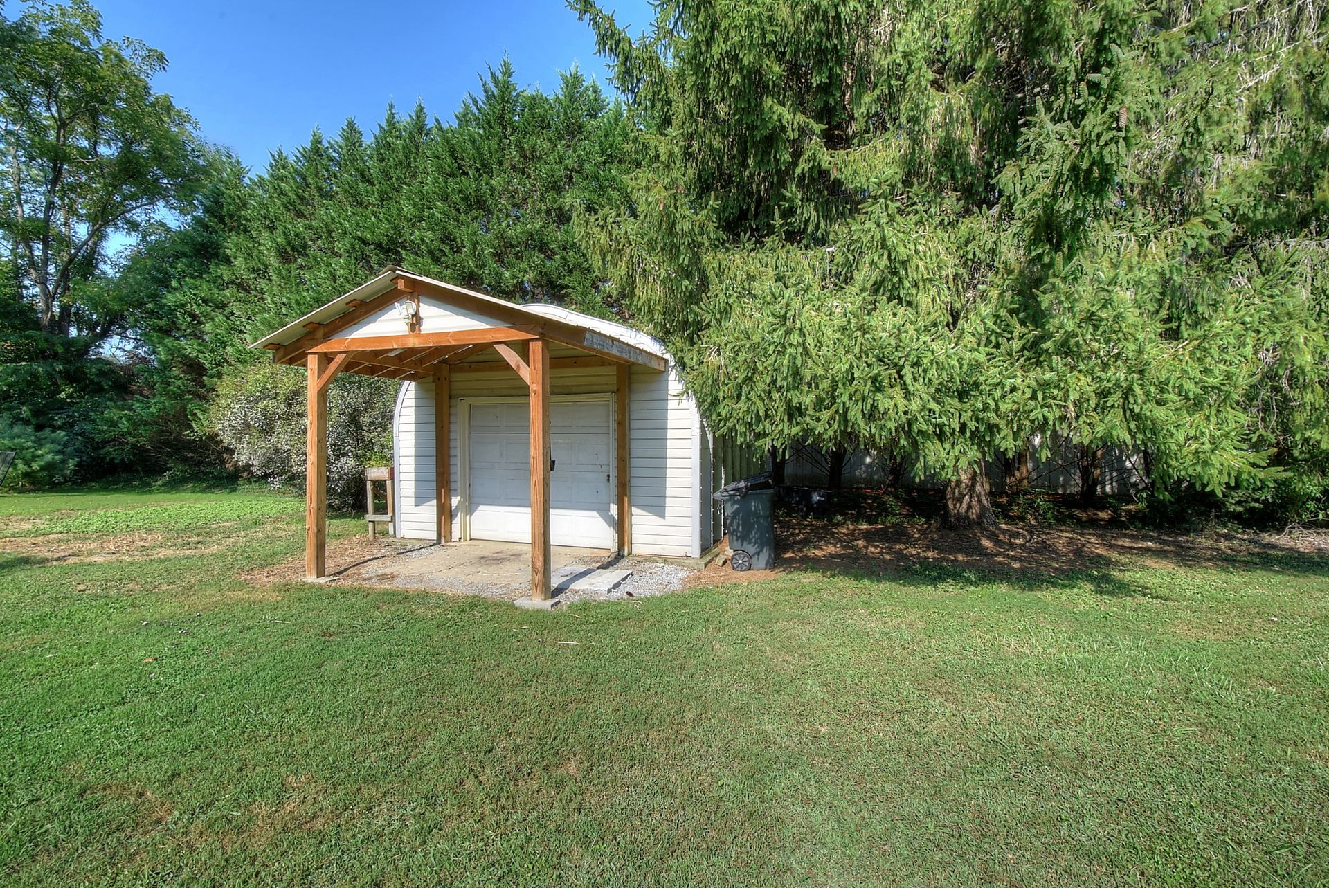 A white shed with a wooden porch is sitting in the middle of a lush green field.