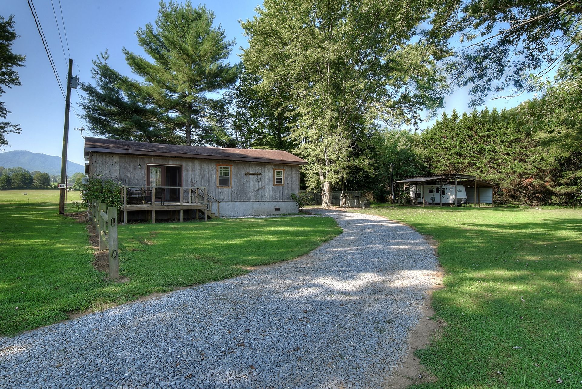 A gravel driveway leads to a small house in the middle of a grassy field.