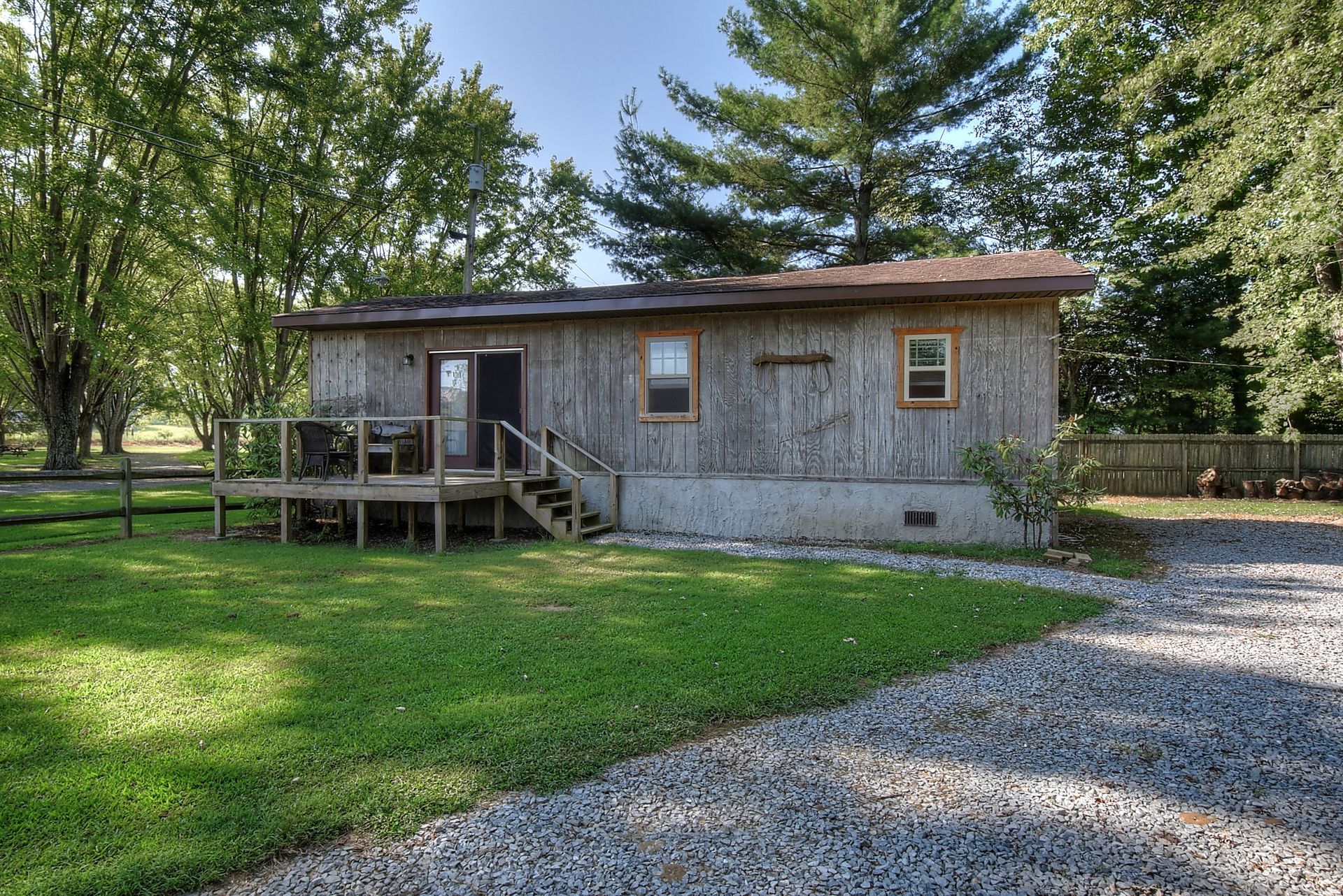 A small wooden house with a deck in the middle of a grassy field.