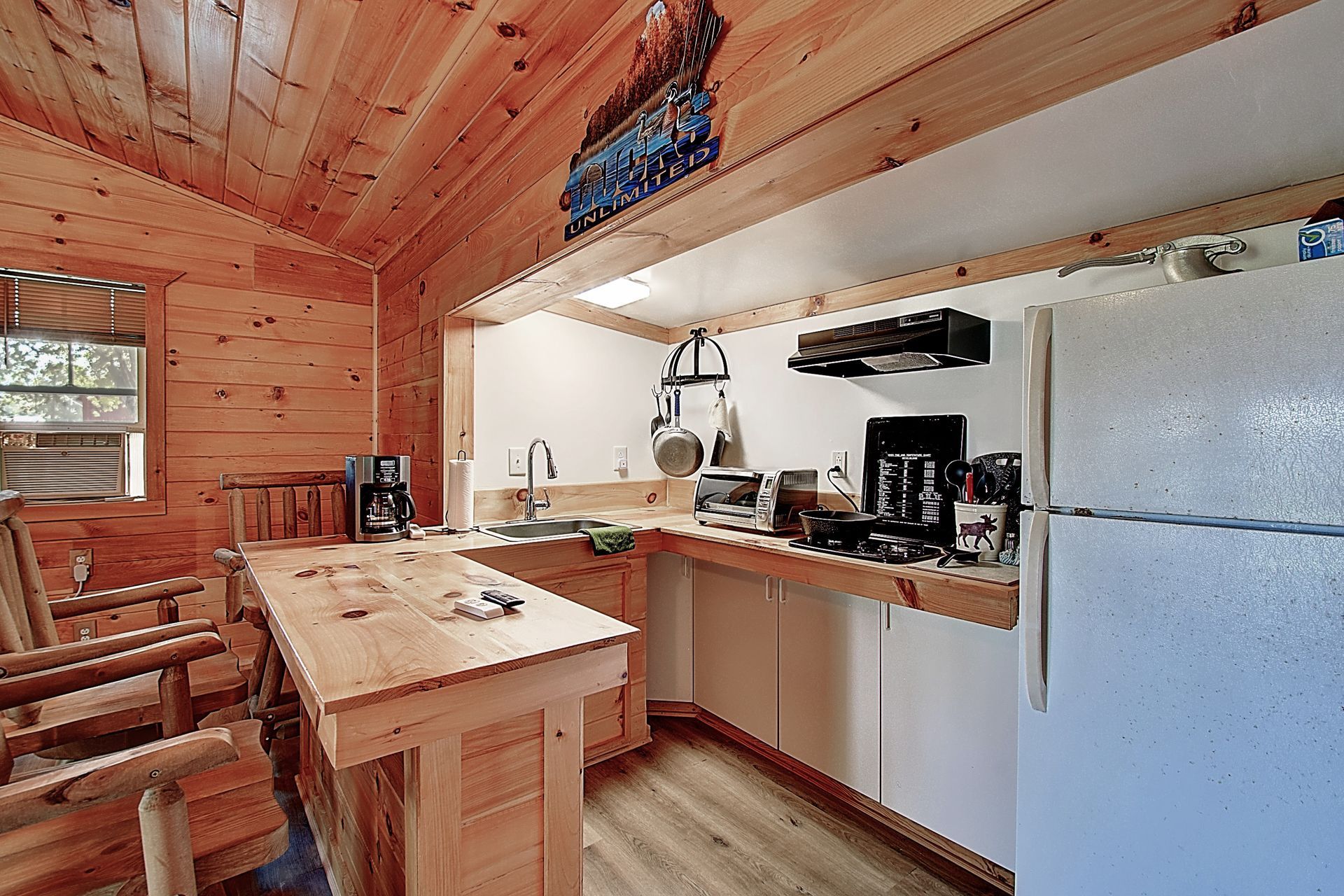 A kitchen in a log cabin with a refrigerator , stove , sink and chairs.
