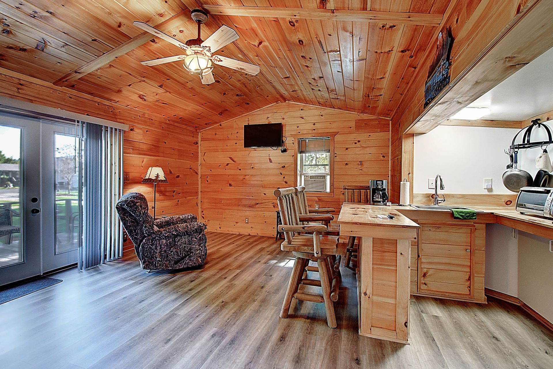 A living room and kitchen in a log cabin with a ceiling fan.