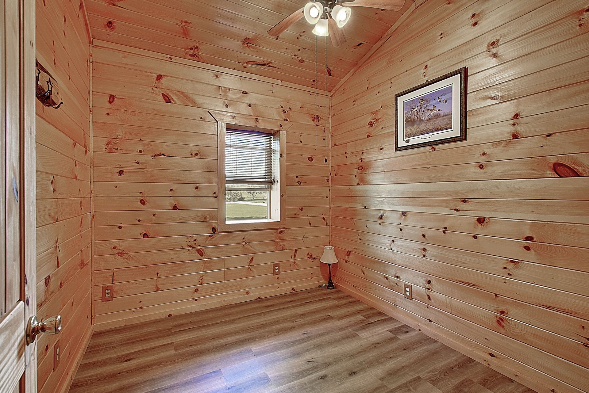 A bedroom in a log cabin with a ceiling fan and a picture on the wall.