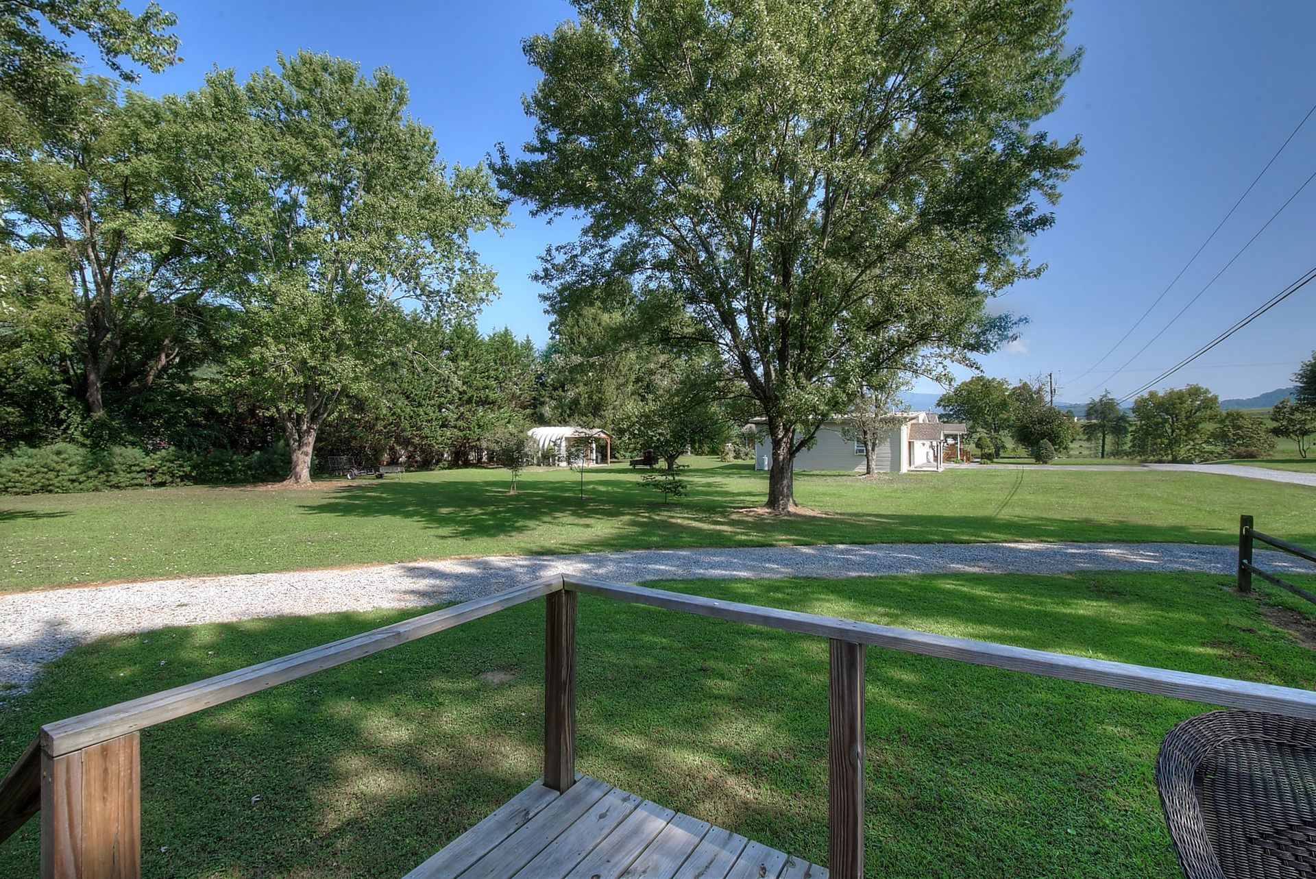 A wooden deck overlooking a grassy field with trees and a house in the background.