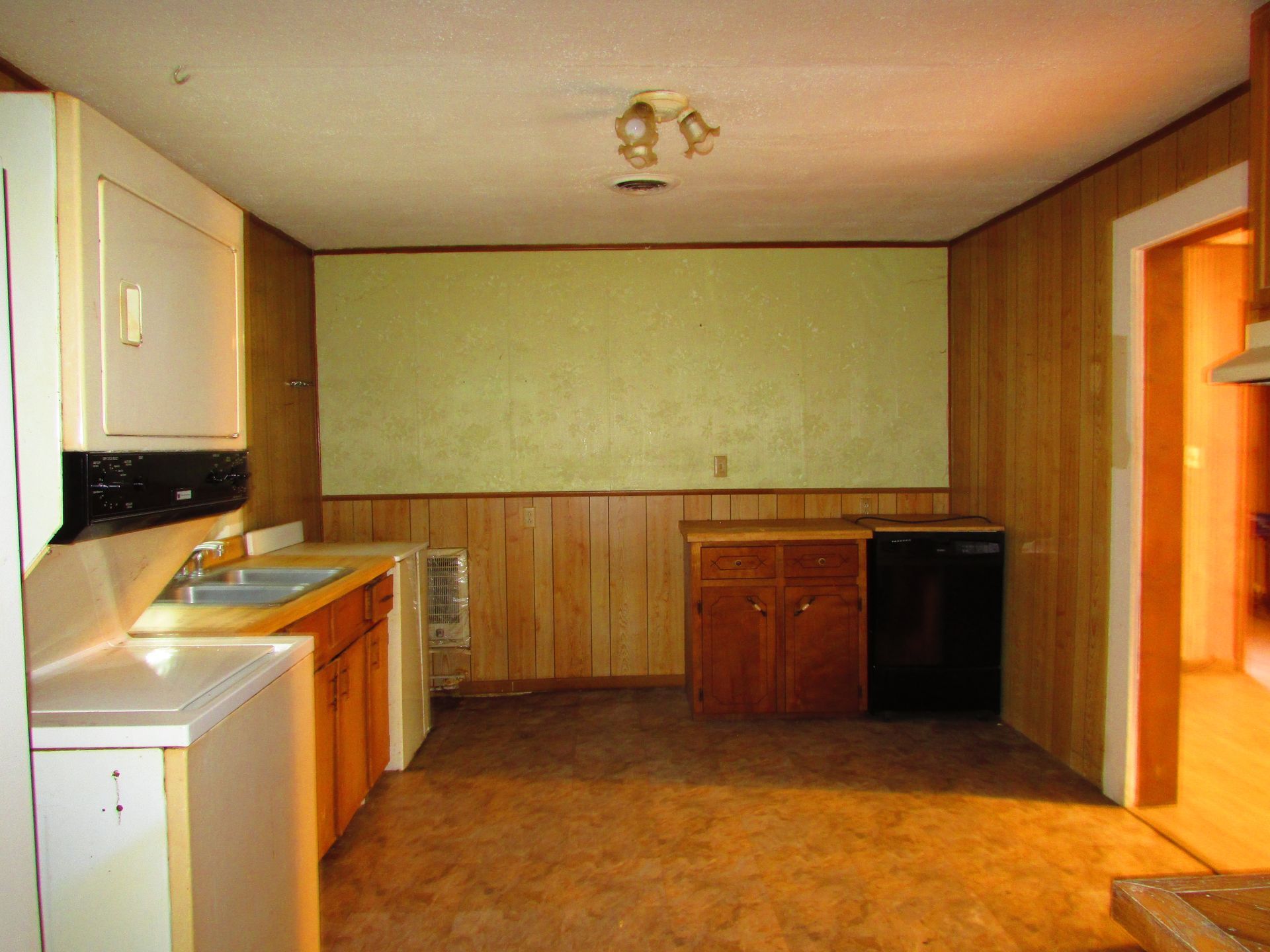 Empty kitchen with wood paneling, countertops, and appliances, viewed from a corner.