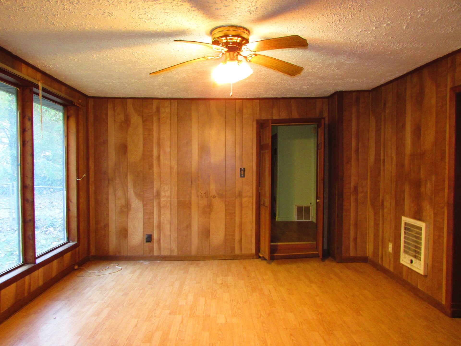 Empty room with wood panel walls, a ceiling fan, windows, and a door.