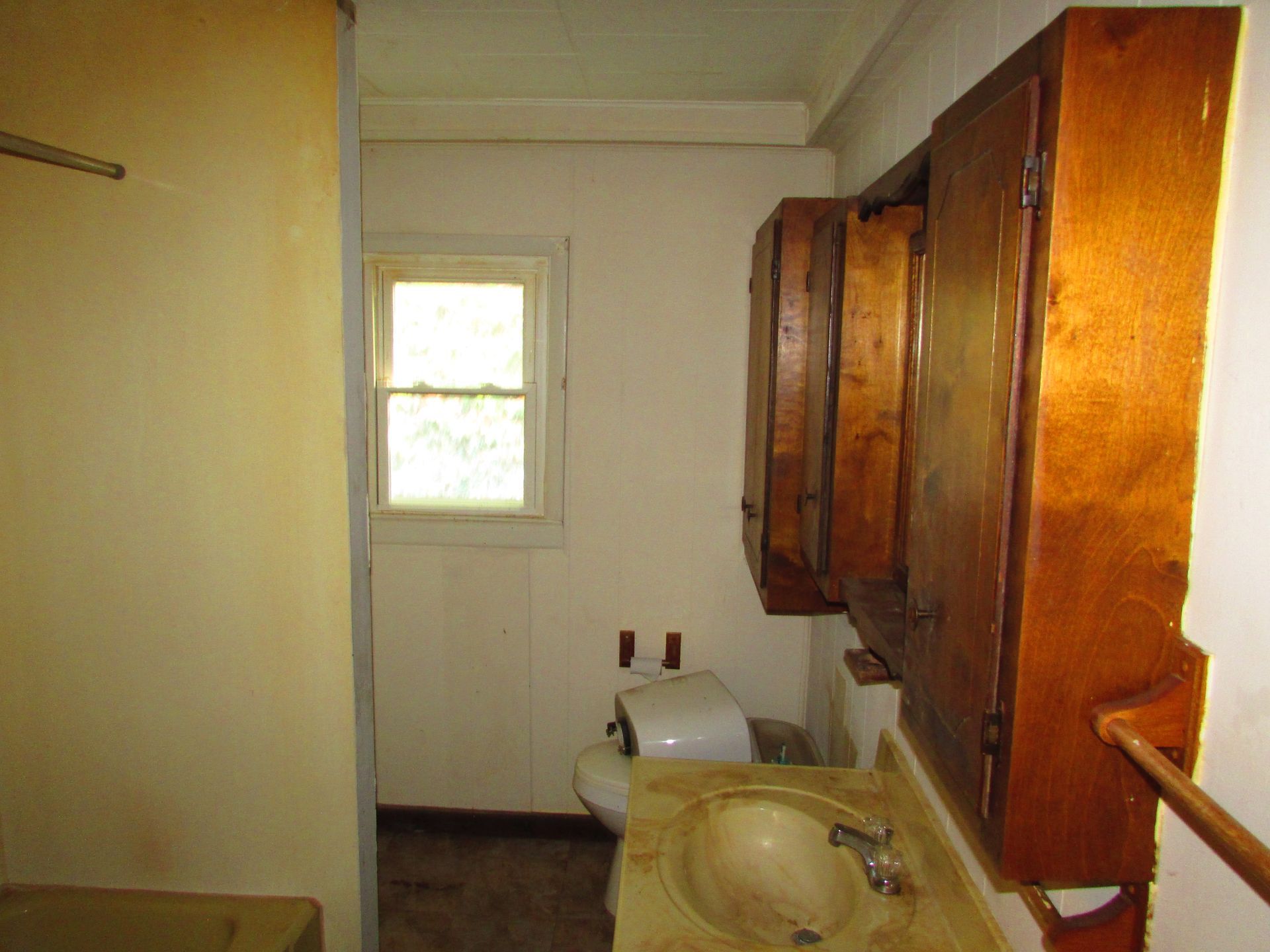 Bathroom with wooden cabinets, a sink, toilet, window, and a towel rack.