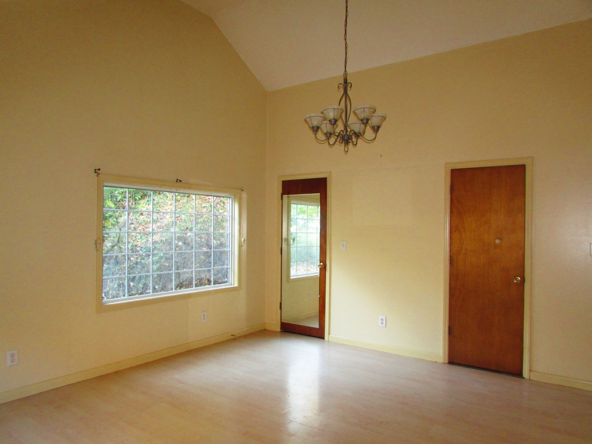 Empty room with pale yellow walls, a window, two doors, and a chandelier.