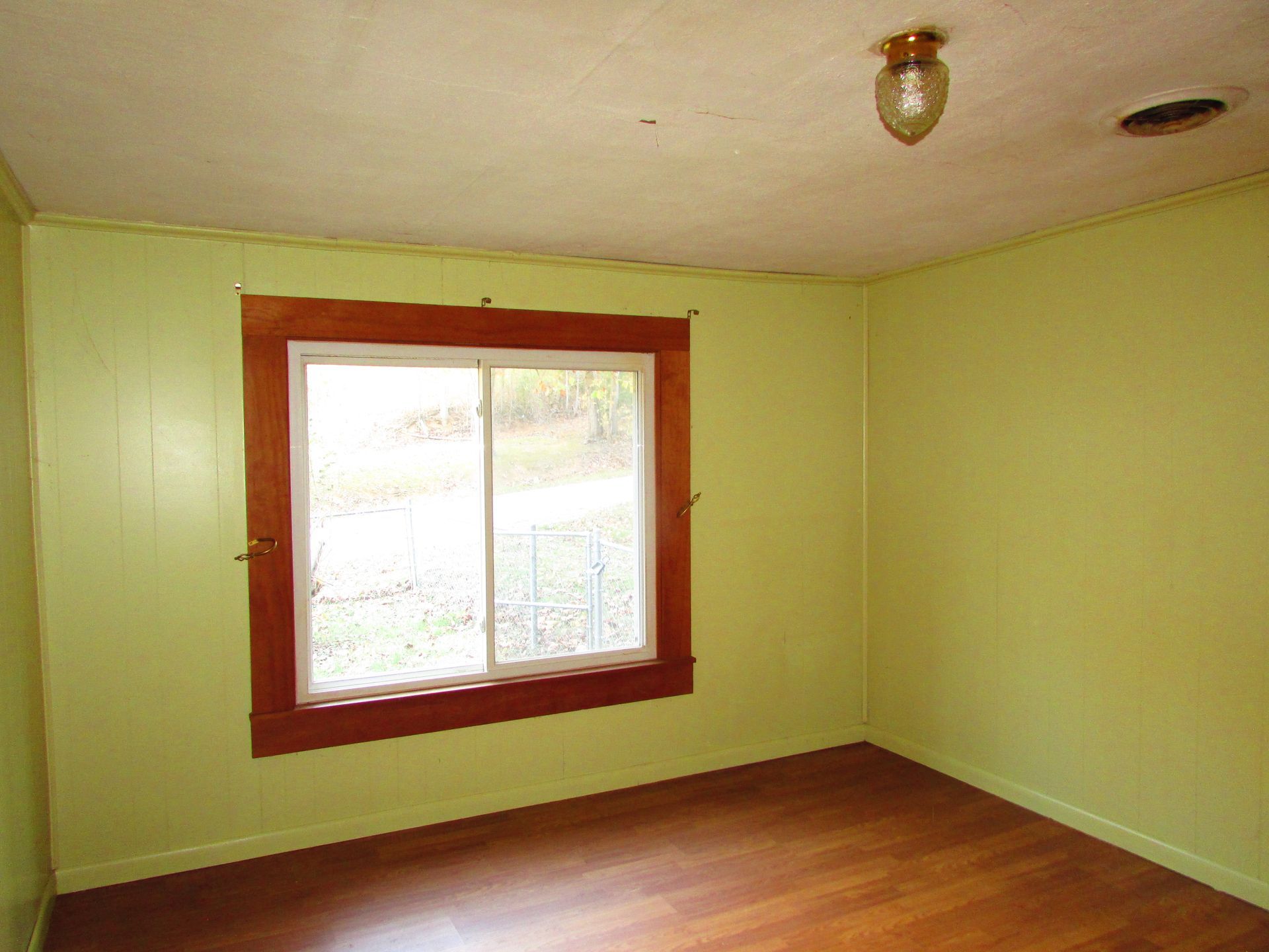 Empty room with light green walls, brown window frame, and hardwood floor.