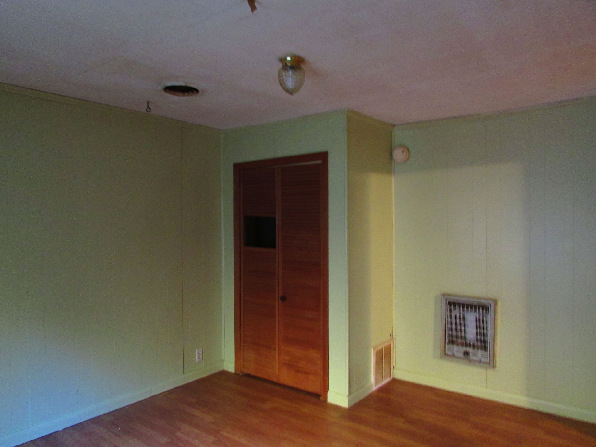 Empty room with green walls, hardwood floor, wooden closet, and a heating unit.
