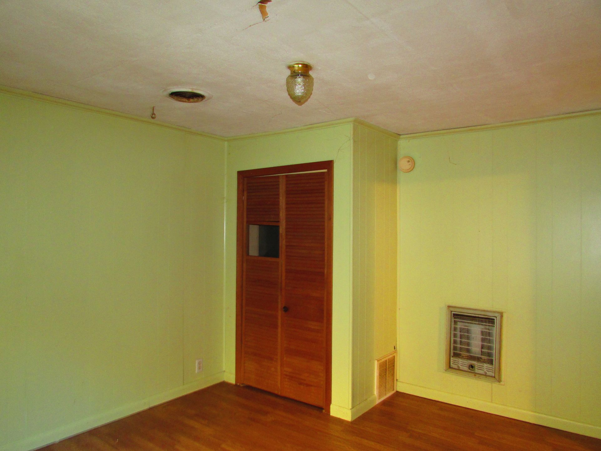 Empty room with light green walls, wooden floor, and a closet.