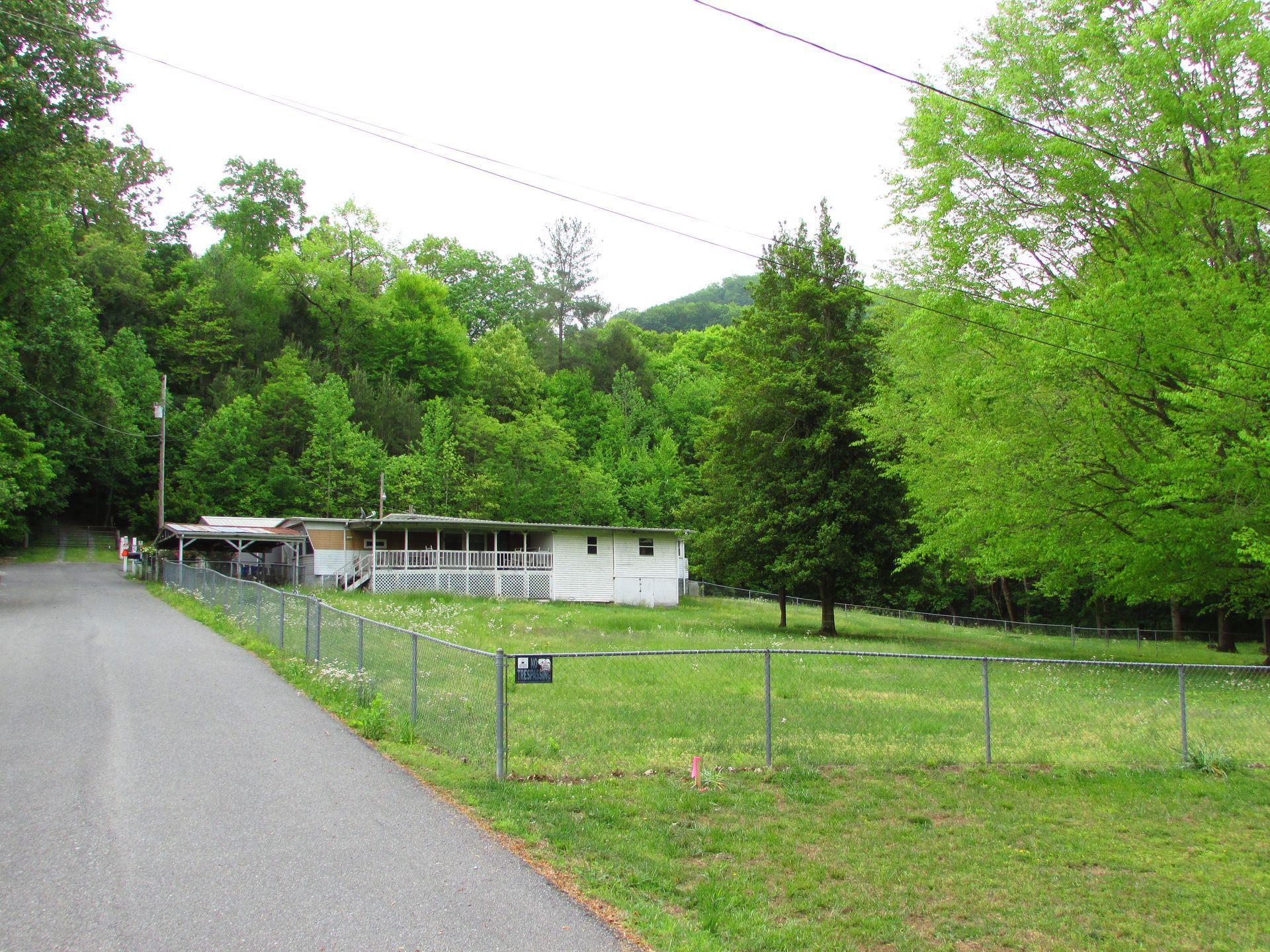 Rural roadside with a small white building, chain-link fence, and lush green trees on a hillside