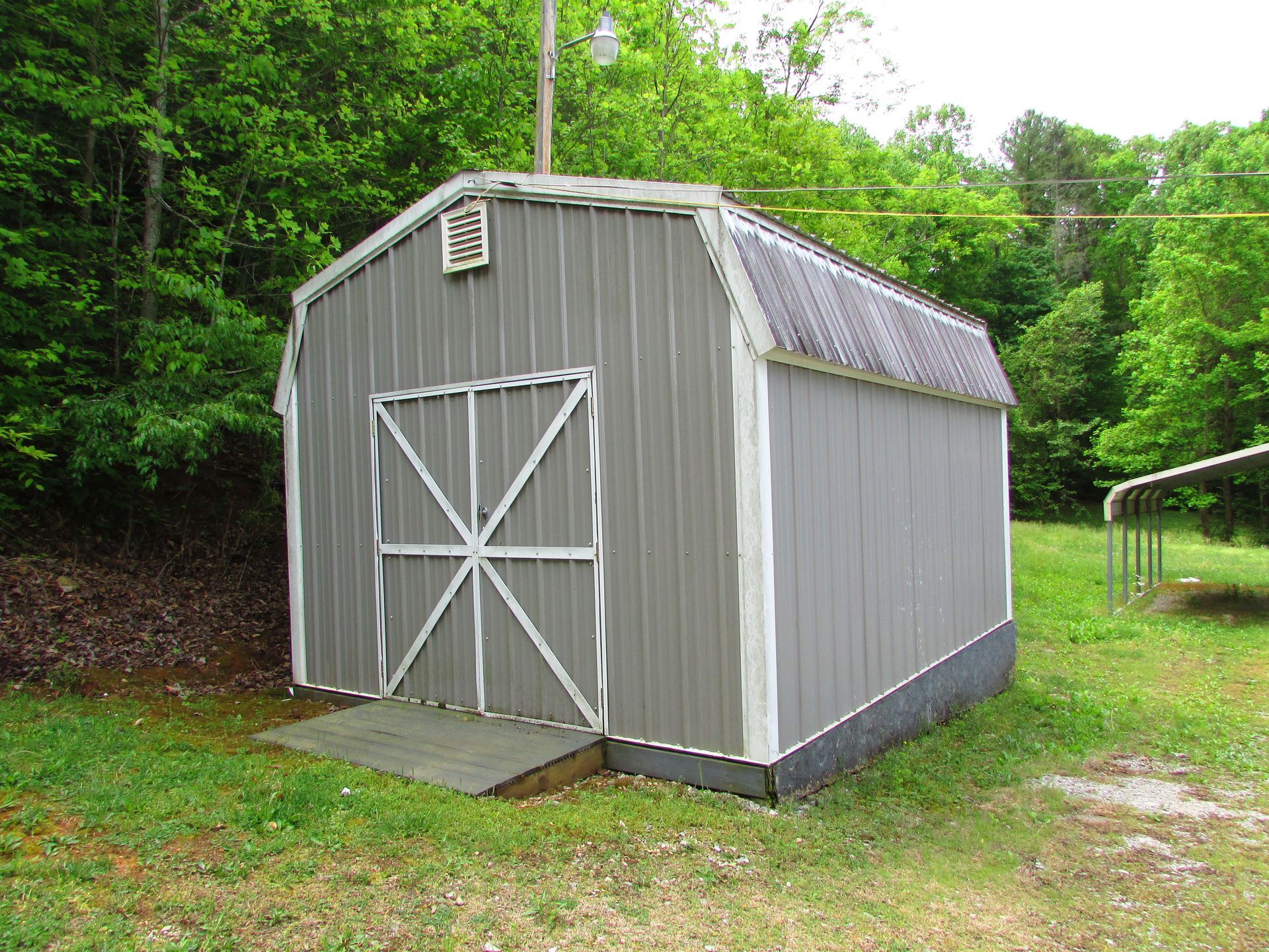 Gray barn shed with white trim in a grassy yard surrounded by trees
