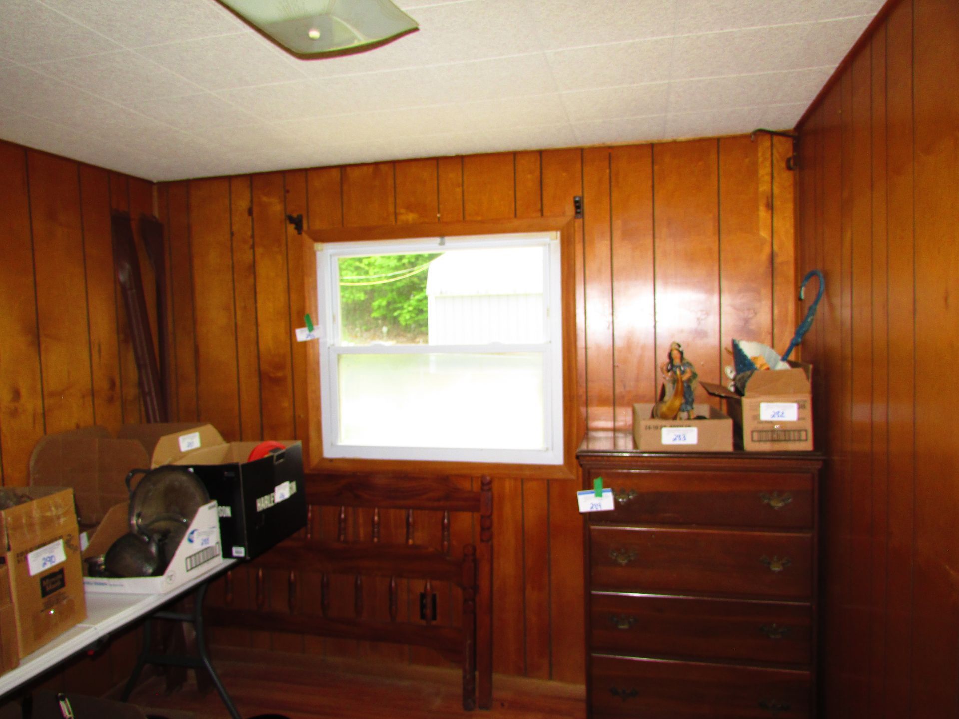 Wood-paneled room with a window, dresser, desk, and assorted tools and boxes on the left.