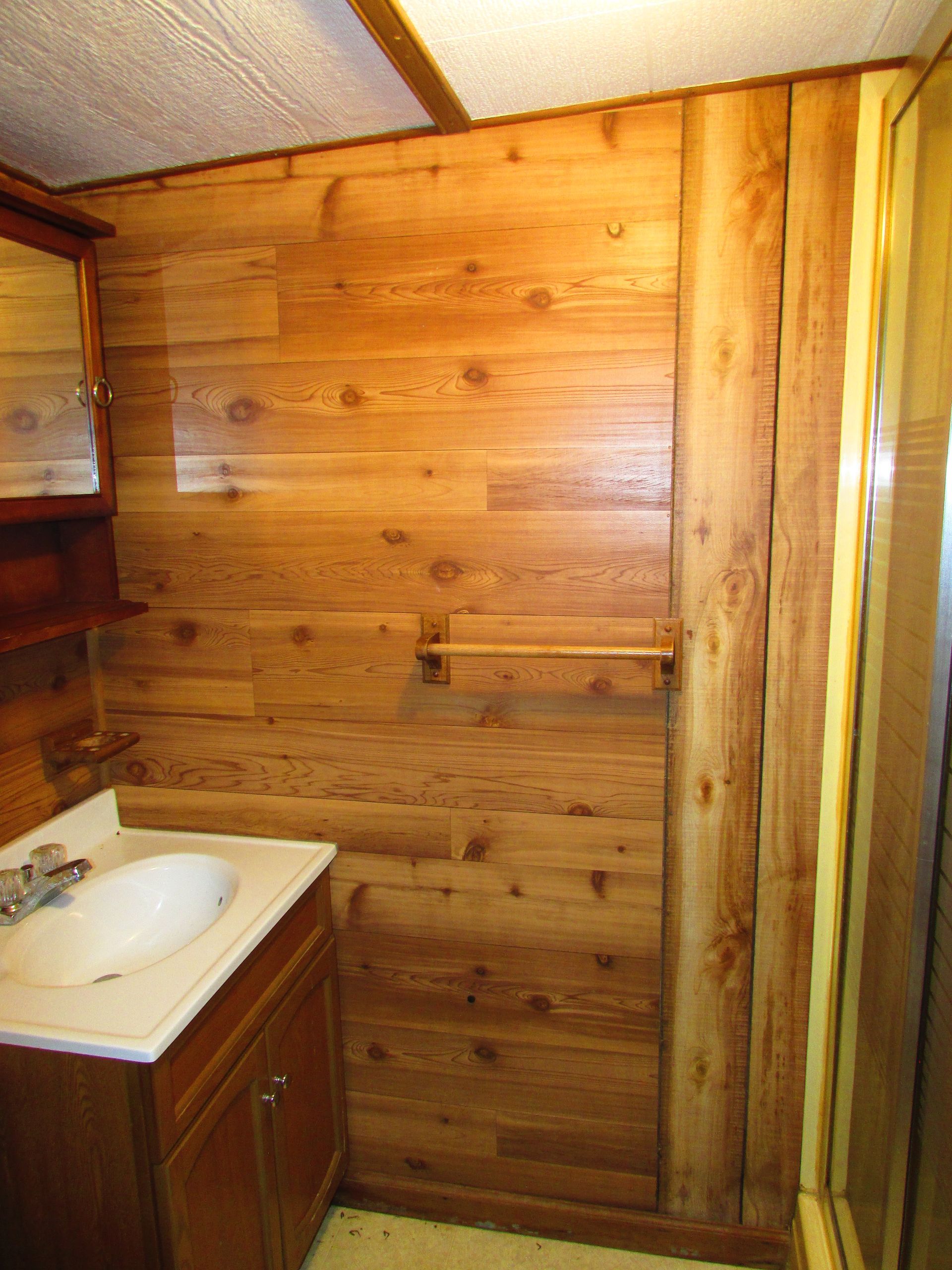 Small wooden bathroom with a sink vanity and shower stall.