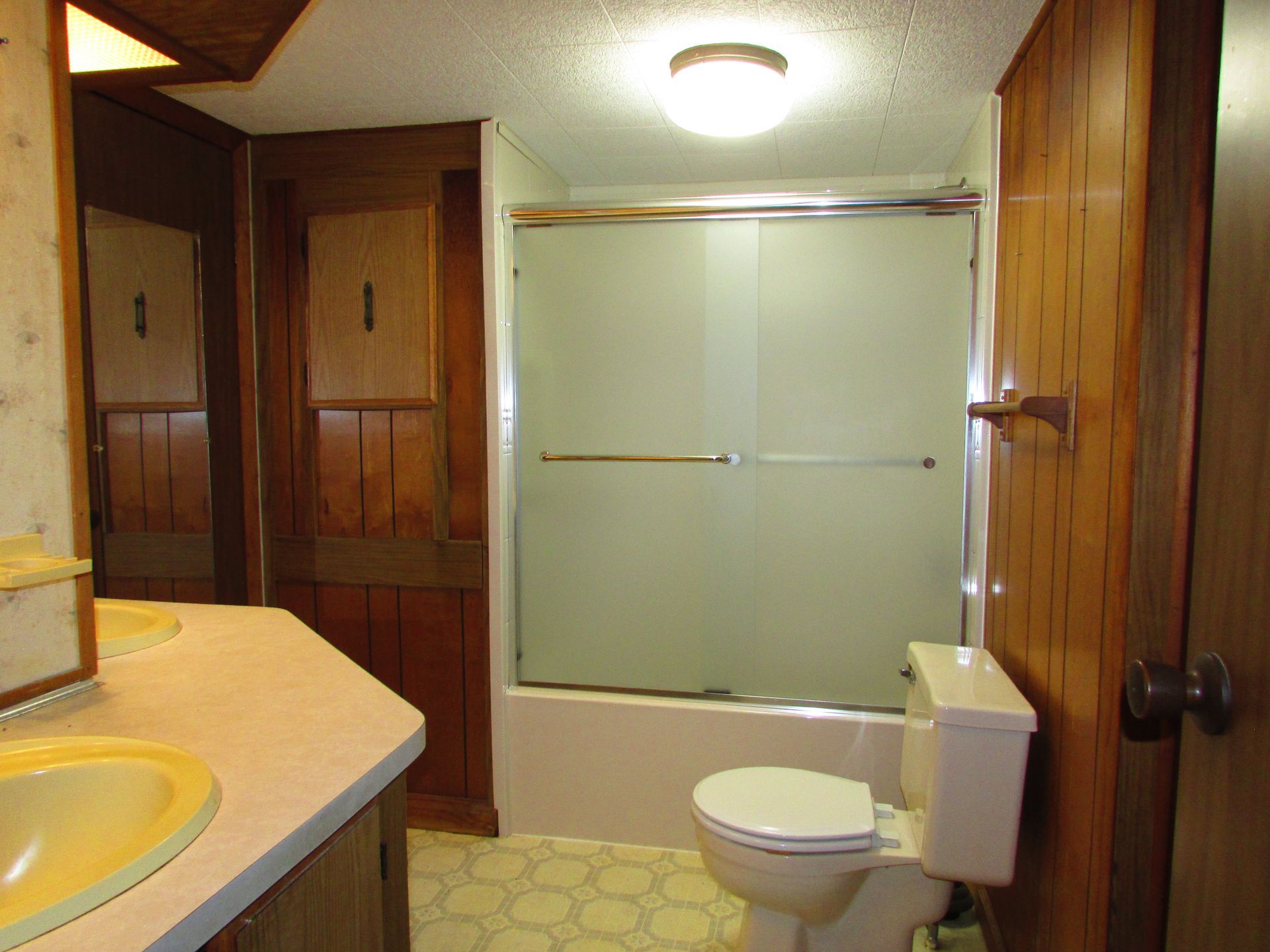 Small wood-paneled bathroom with sink, toilet, and frosted glass shower enclosure.