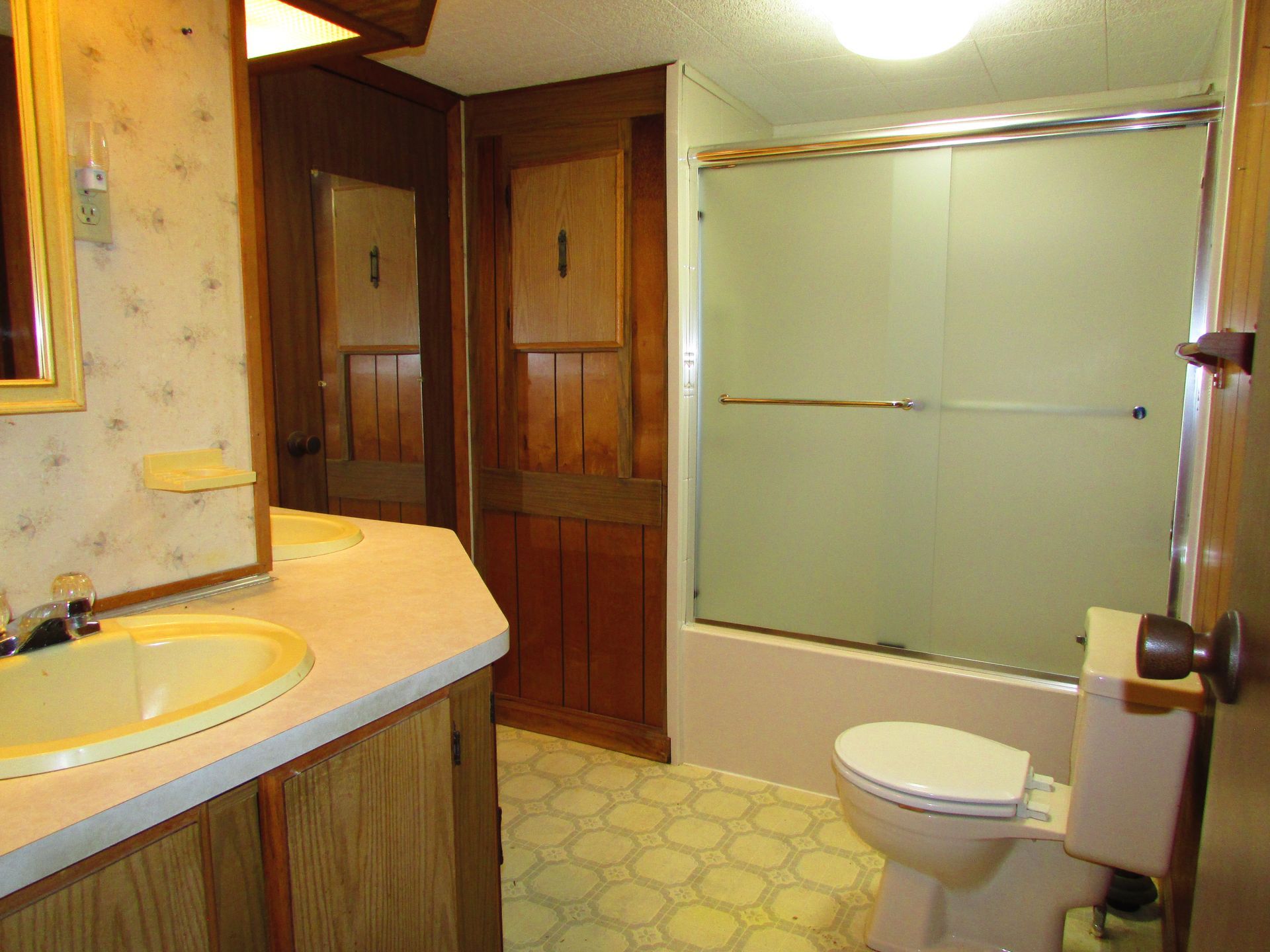 Bathroom with sink, toilet, and frosted glass shower door in a wood-paneled interior