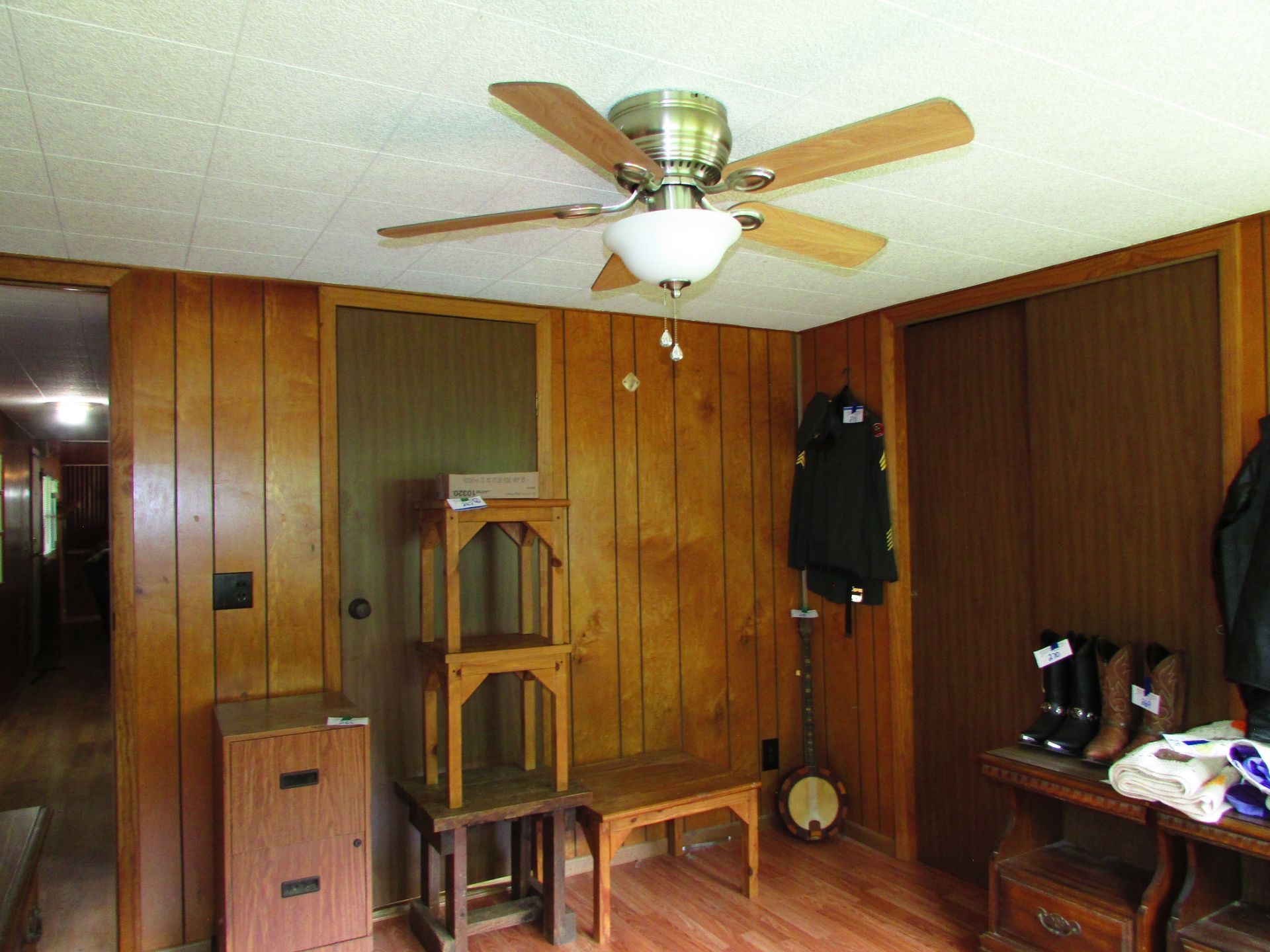 Wood-paneled room with a ceiling fan, dresser, coat rack, small table, and hanging clothes