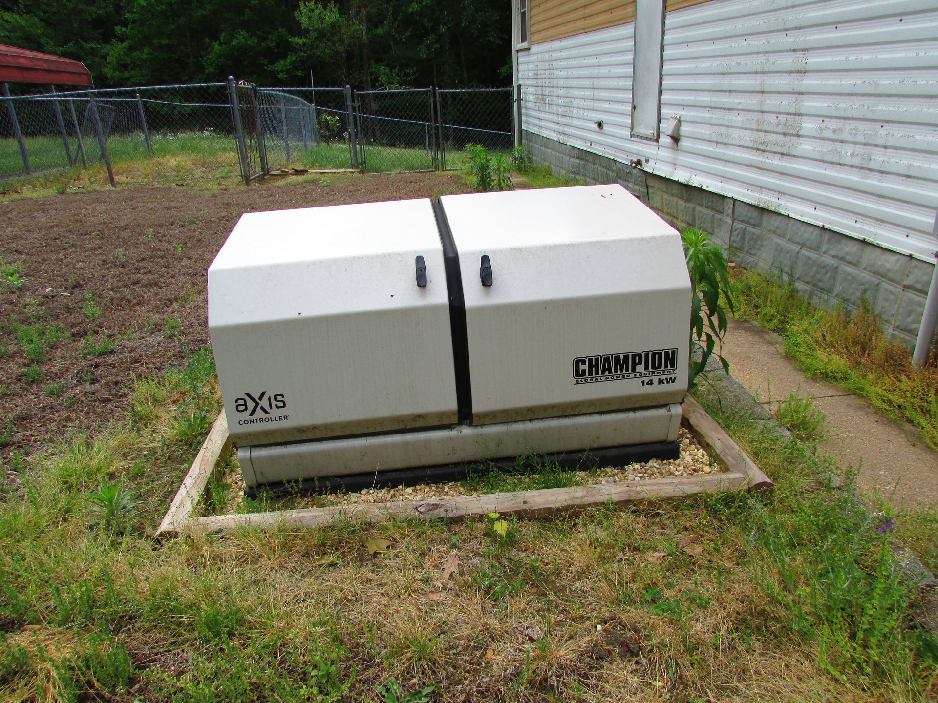 White utility box in a backyard beside a house, surrounded by grass and a garden bed.