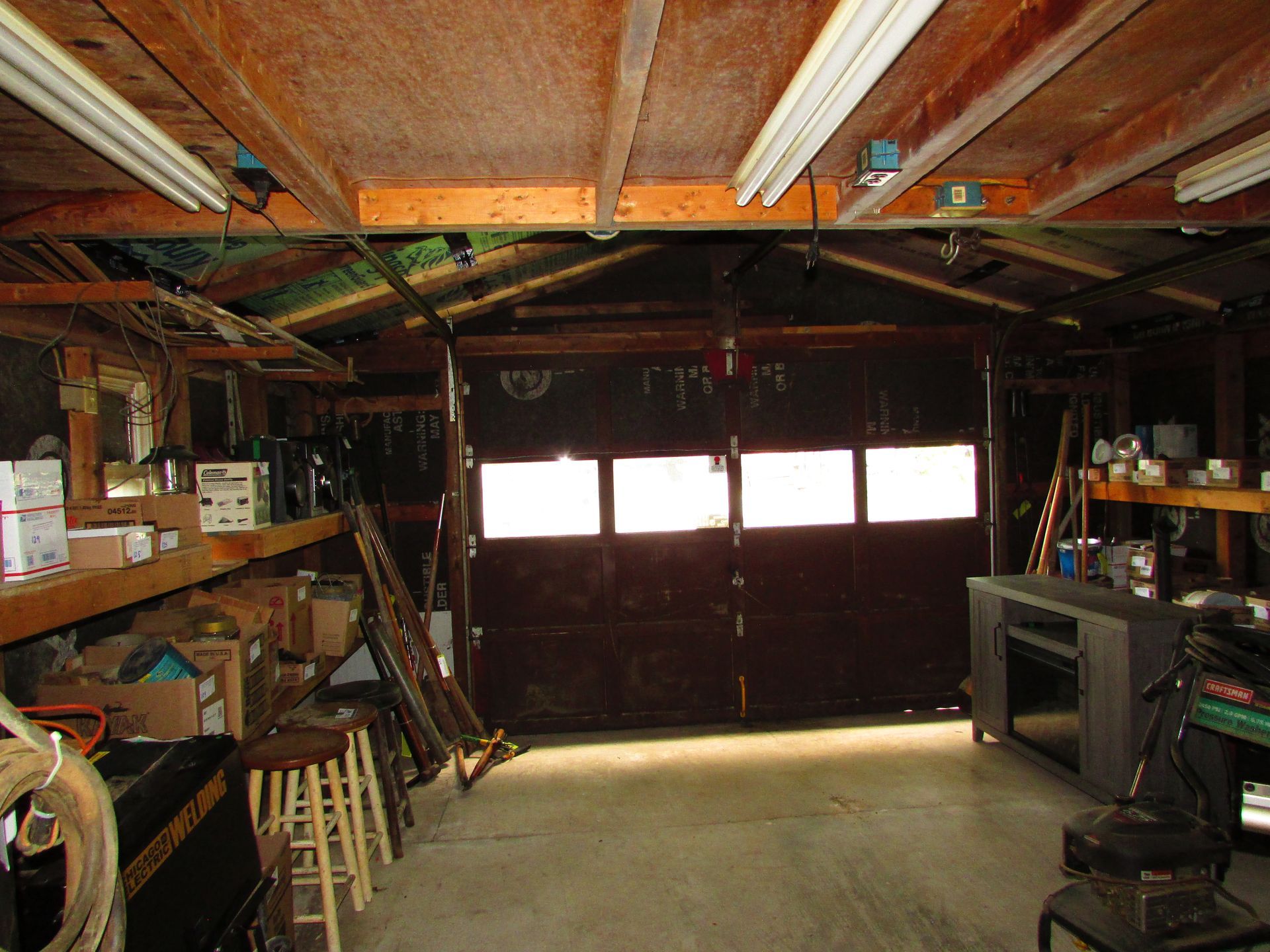 Dim garage workshop with shelves, tools, and a closed wooden door with windows.