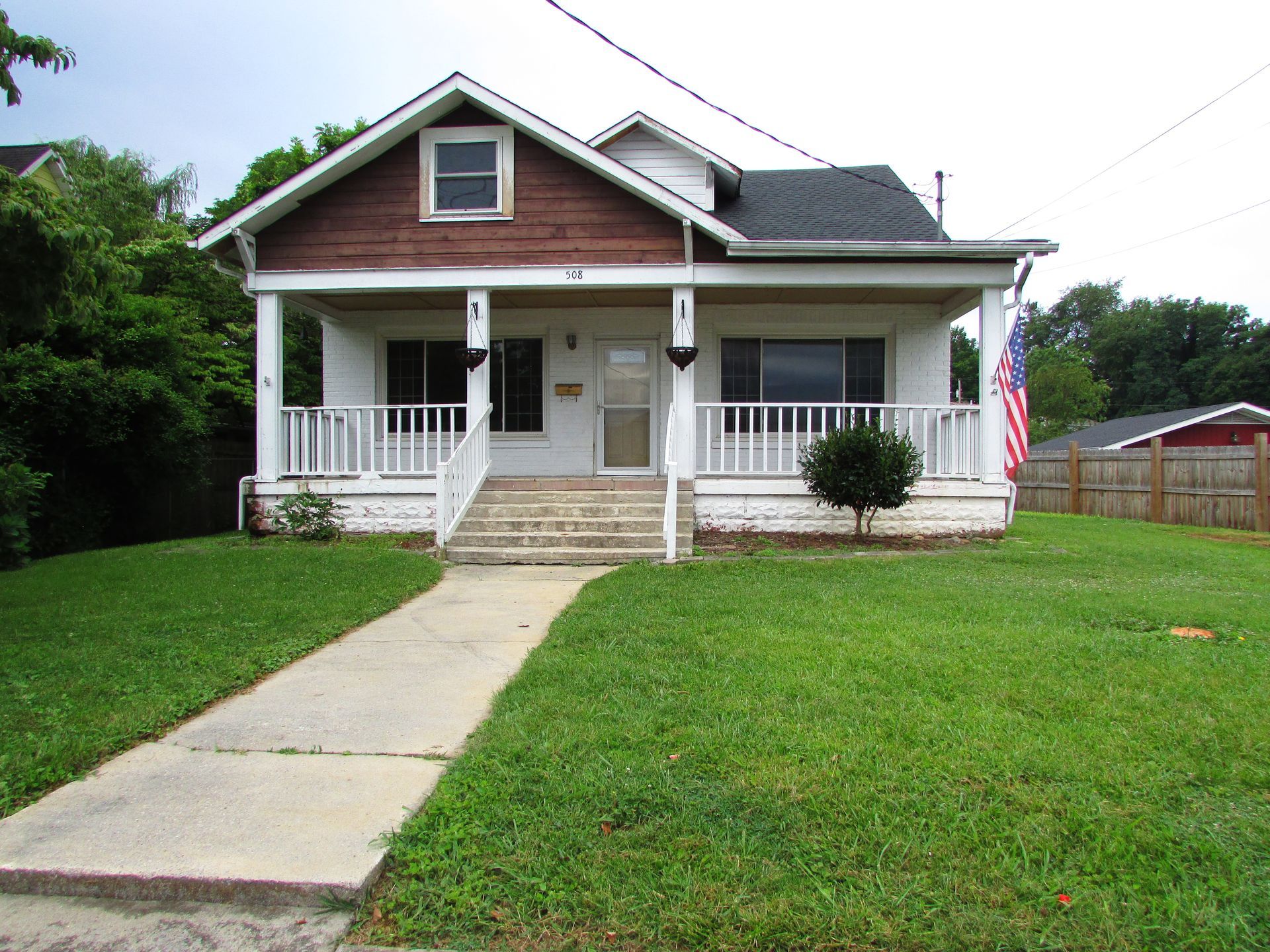 Small house with white porch, green lawn, and concrete walkway in a suburban yard.