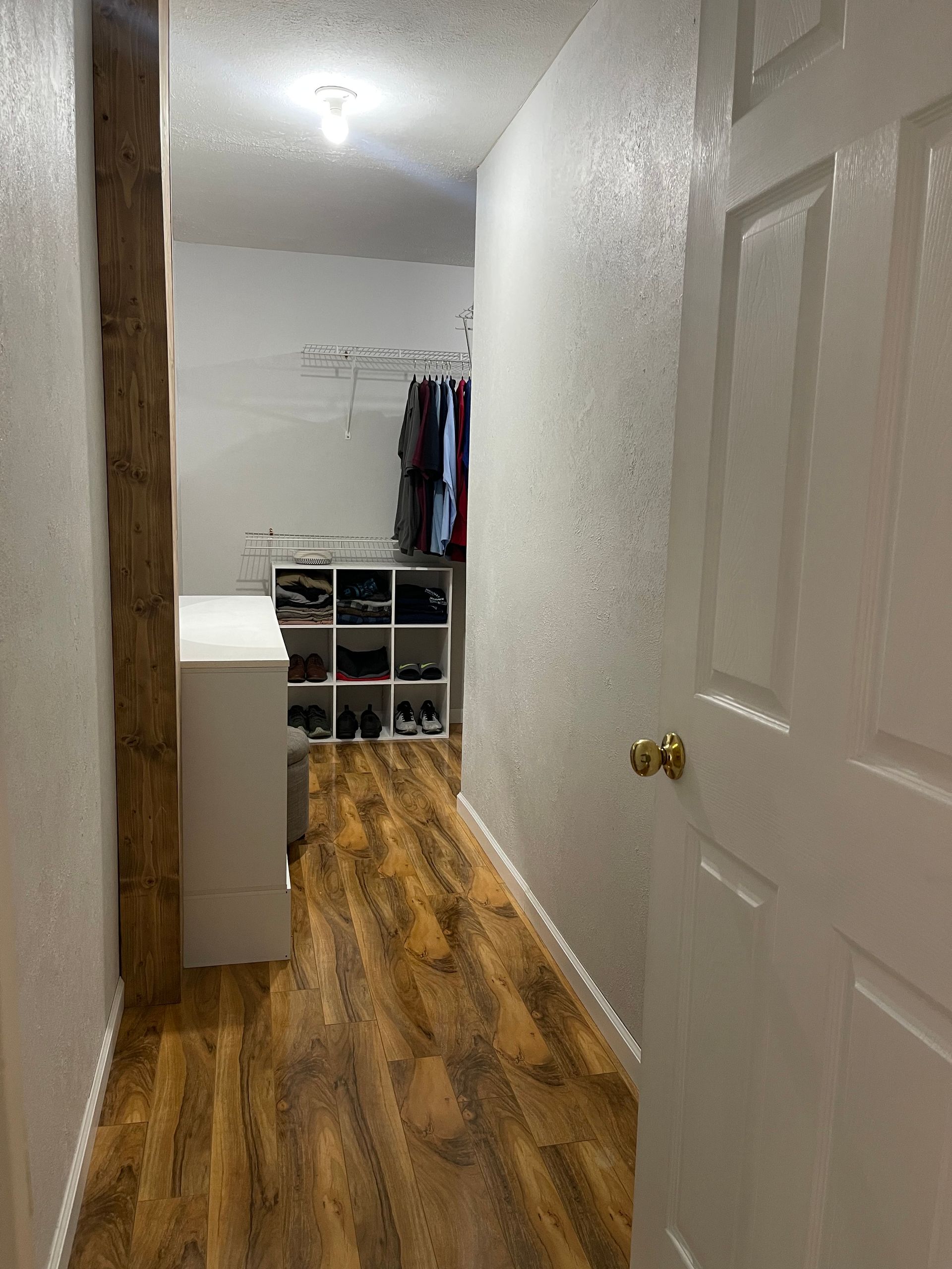 A hallway with hardwood floors and a white door leading to a closet.