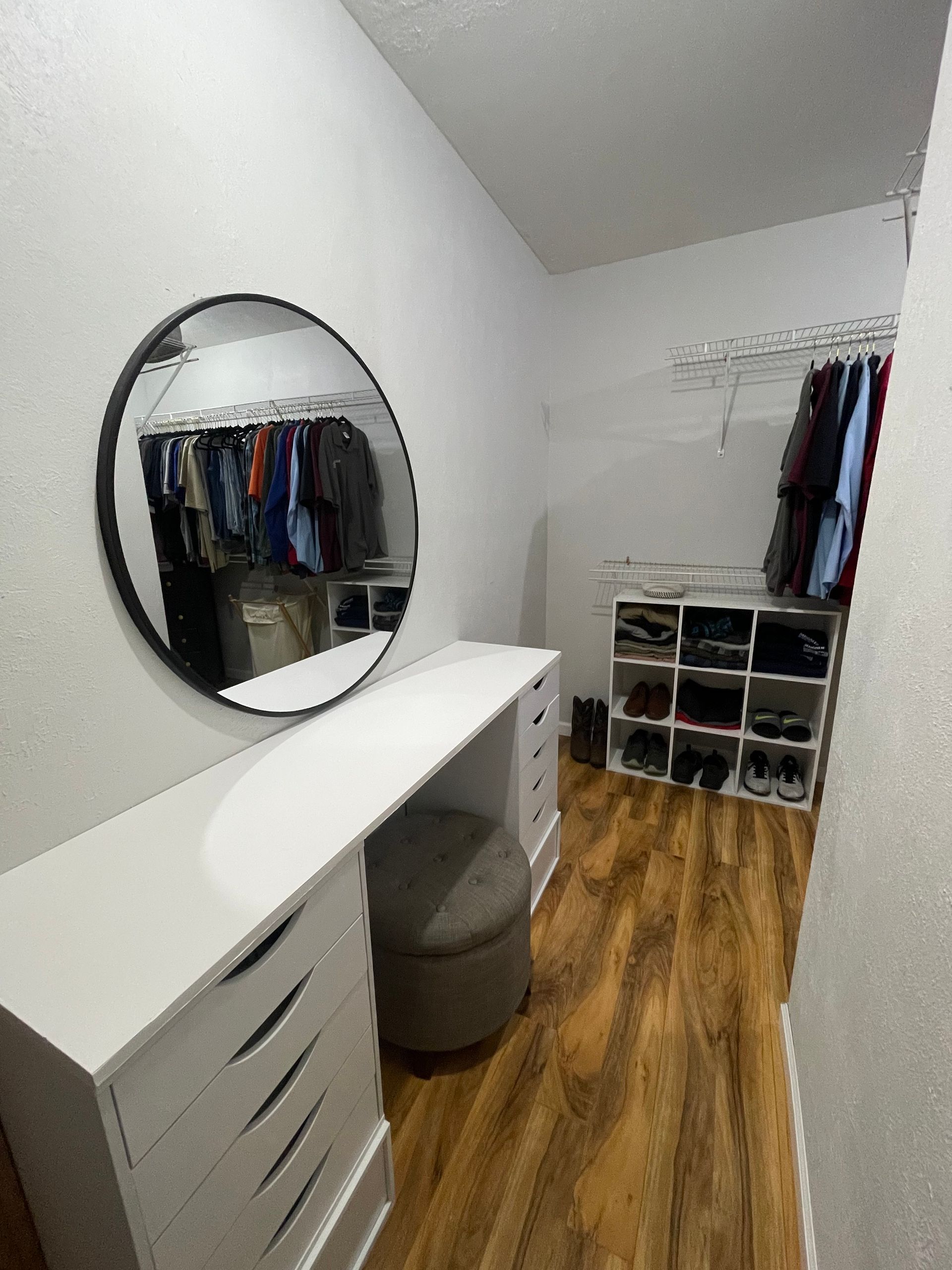 A walk in closet with a round mirror and a desk.