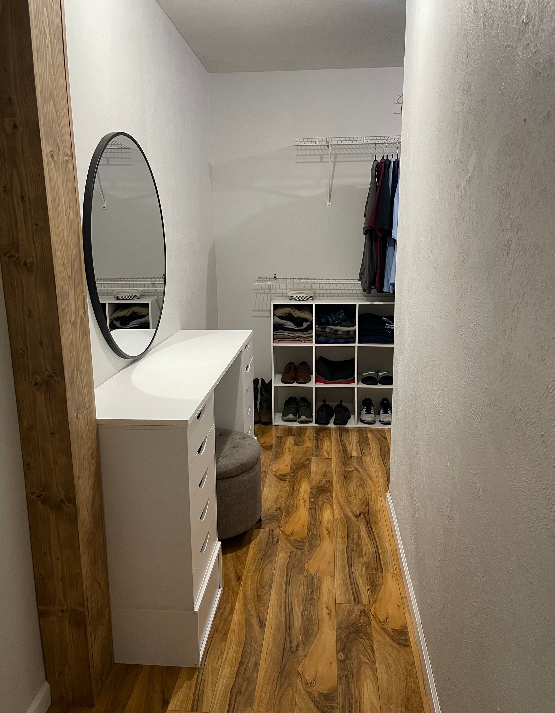 A walk in closet with a mirror , dresser , and ottoman.
