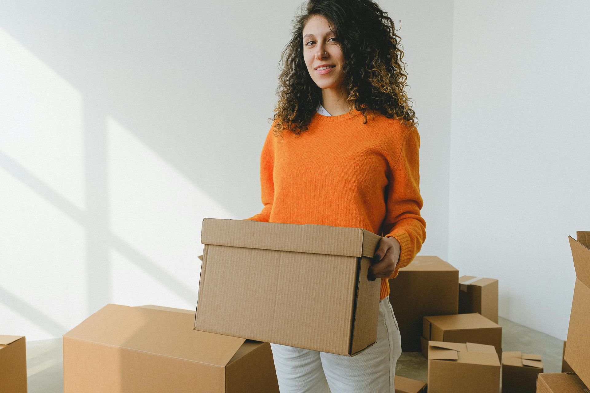 A woman home buyer is holding a cardboard box while moving into a new house she just bought