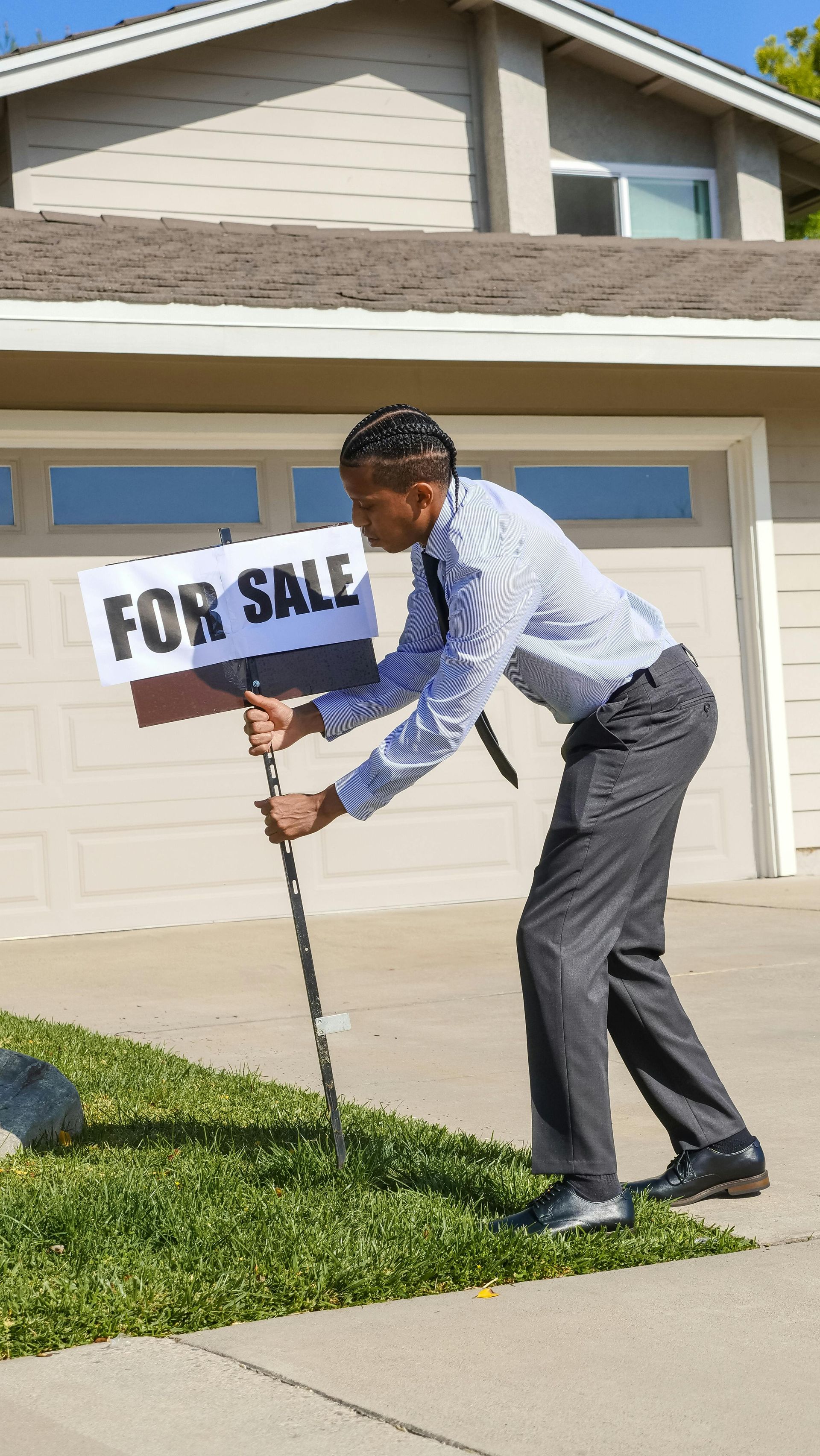 A man is holding a for sale sign in front of a house.