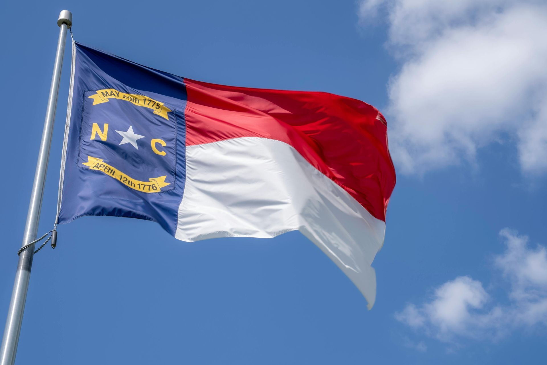North Carolina state flag waving in the wind against a blue sky.
