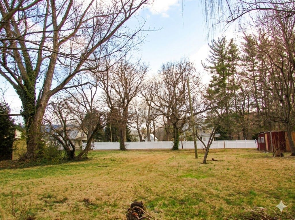 Brown grassy field with bare trees, white fence, and cloudy blue sky.