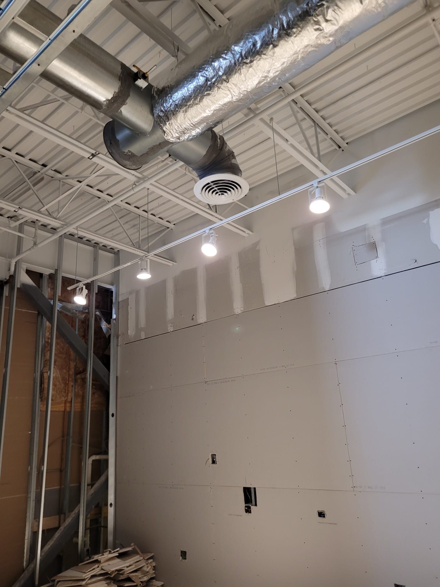 Interior of a building under construction, drywall and exposed metal beams with ceiling vents and lights.