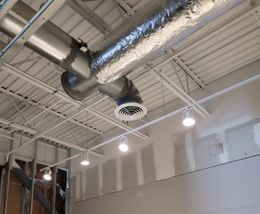 HVAC ductwork and ceiling lights in a construction setting. White ceiling and unfinished walls are visible.