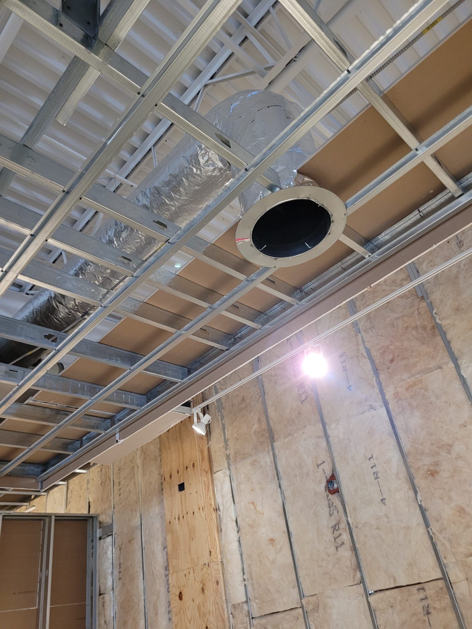 Metal grid ceiling with a circular opening, likely for HVAC. Wood-paneled wall.