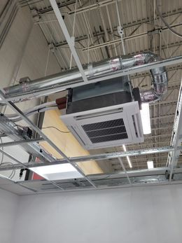 Ceiling-mounted air conditioning unit in a building. Metal framing supports the unit and ductwork.