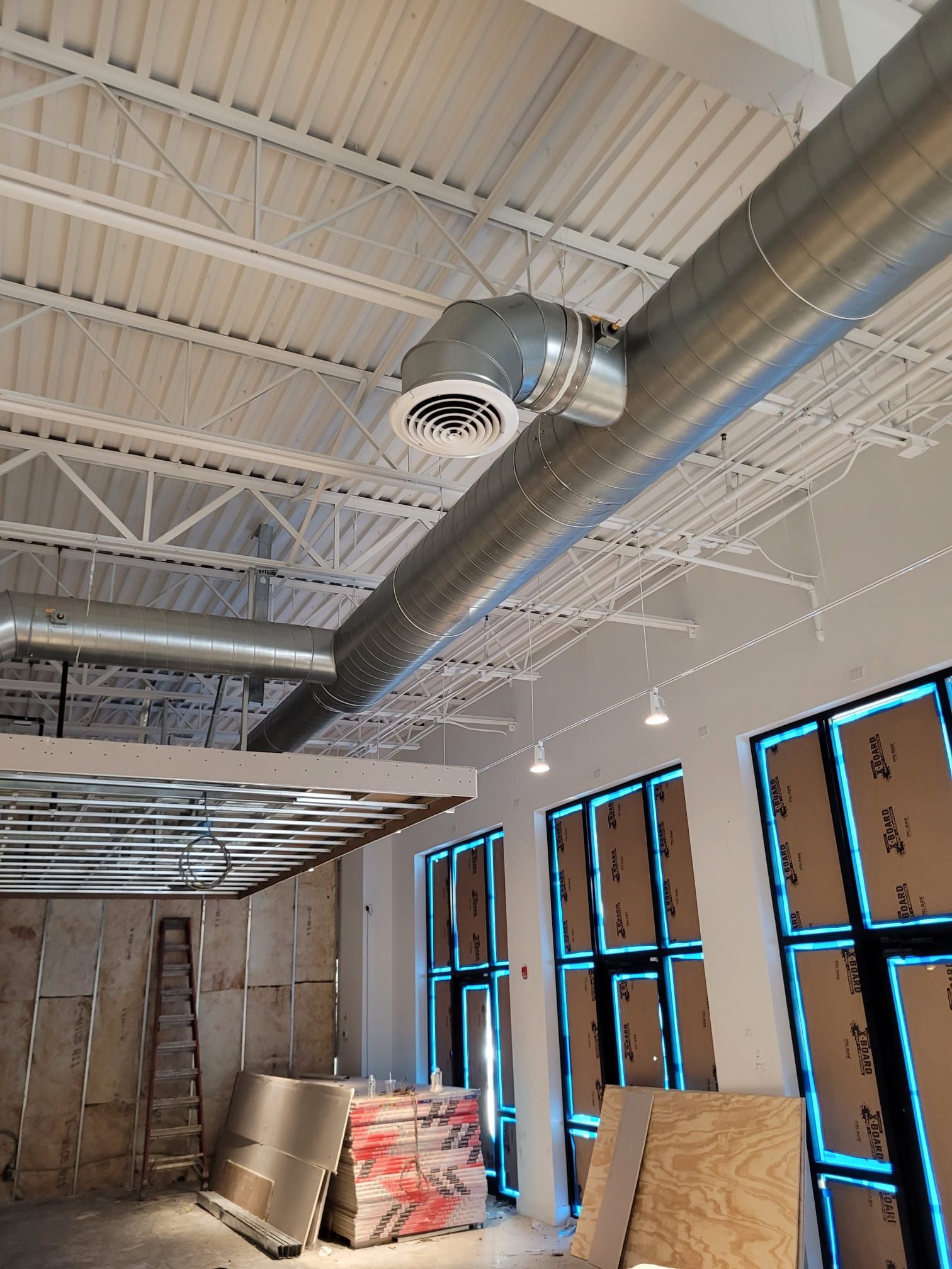 HVAC ductwork installation in a construction site. Metal ducts run across the ceiling, near windows.