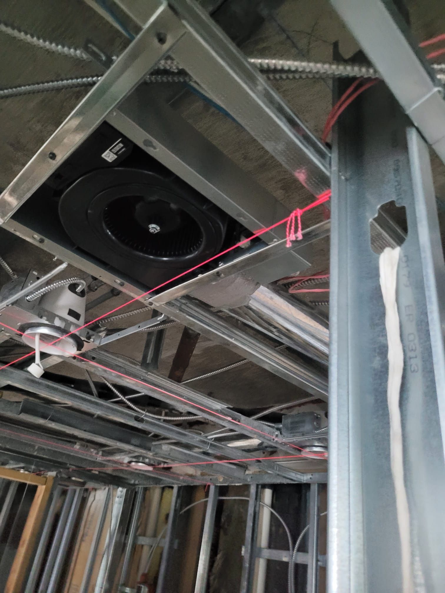 Construction site ceiling with metal framing, wires, and a black circular object.
