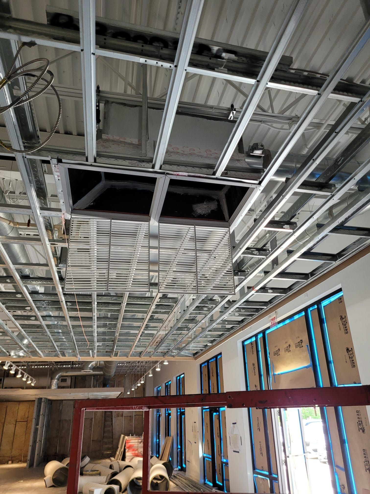 Construction site interior; metal ceiling framework with open access panels, unfinished windows, and red door frame.