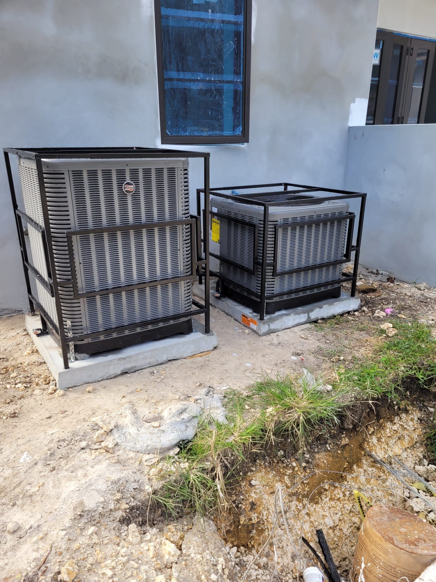 Two outdoor air conditioning units with protective metal cages, near a building.